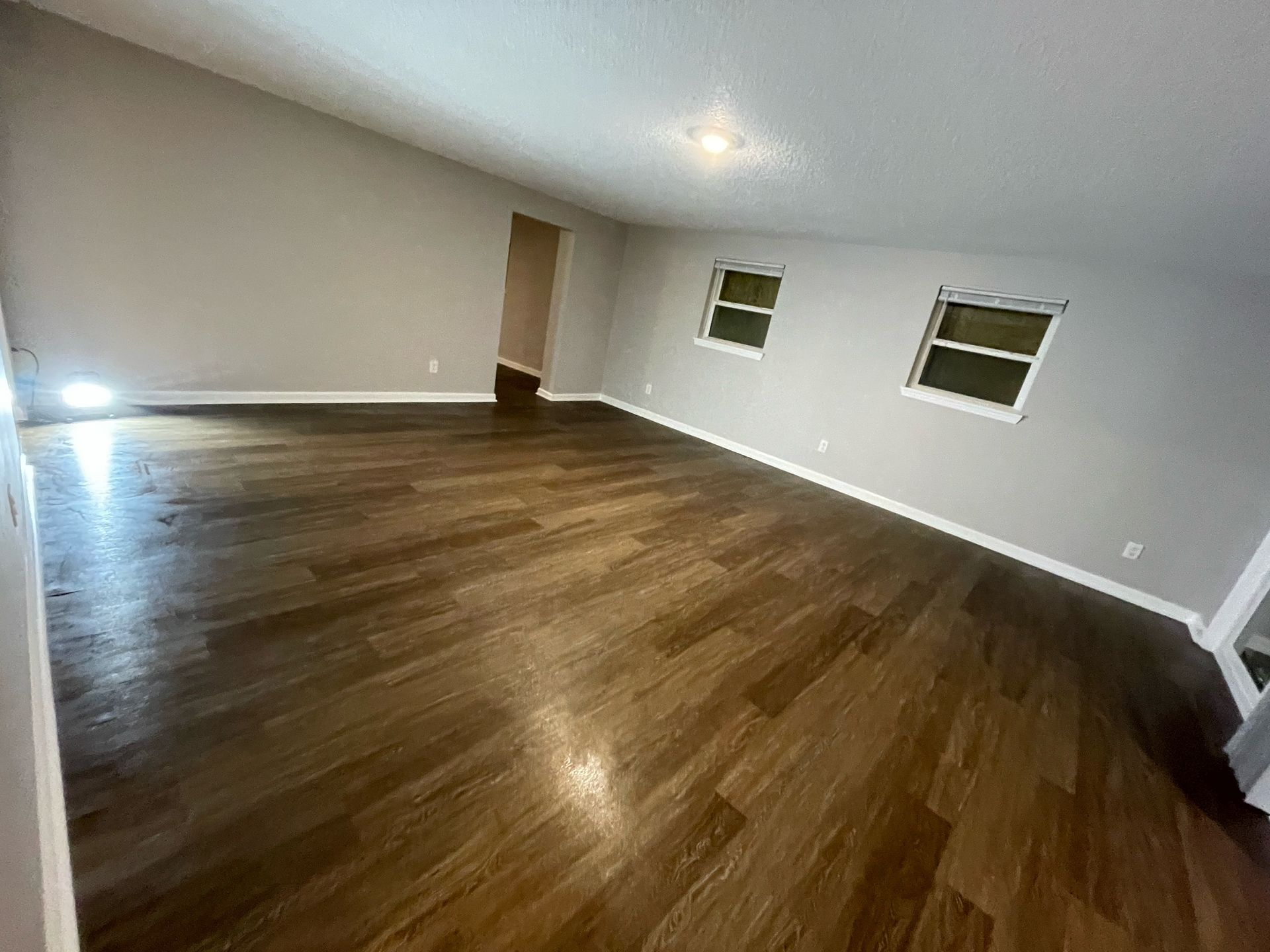 Empty room with dark wood floors, gray walls, and two windows; a doorway is visible in the distance.