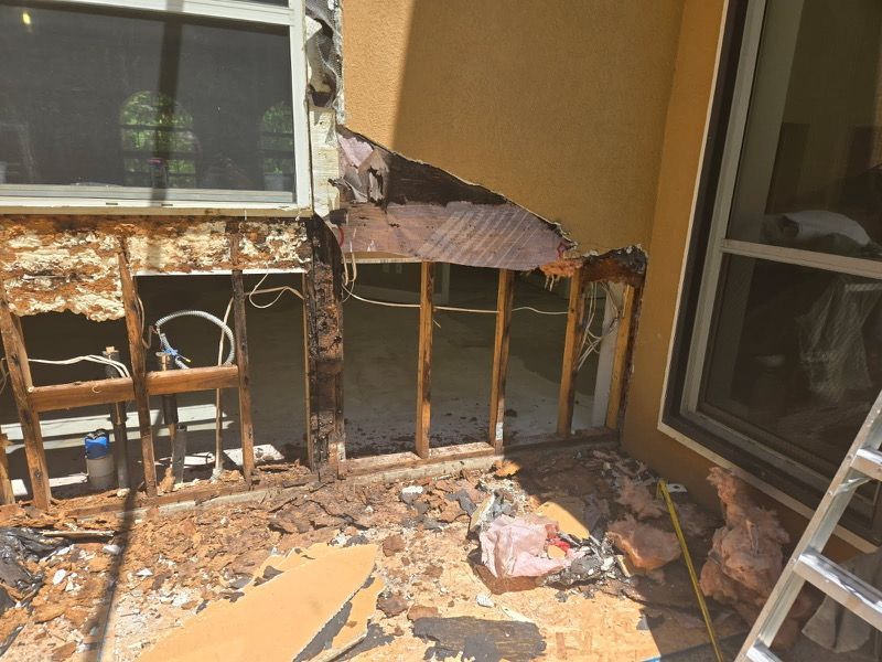 Exterior wall damage exposing wooden framing, wiring, and insulation near a window. Debris litters the ground.