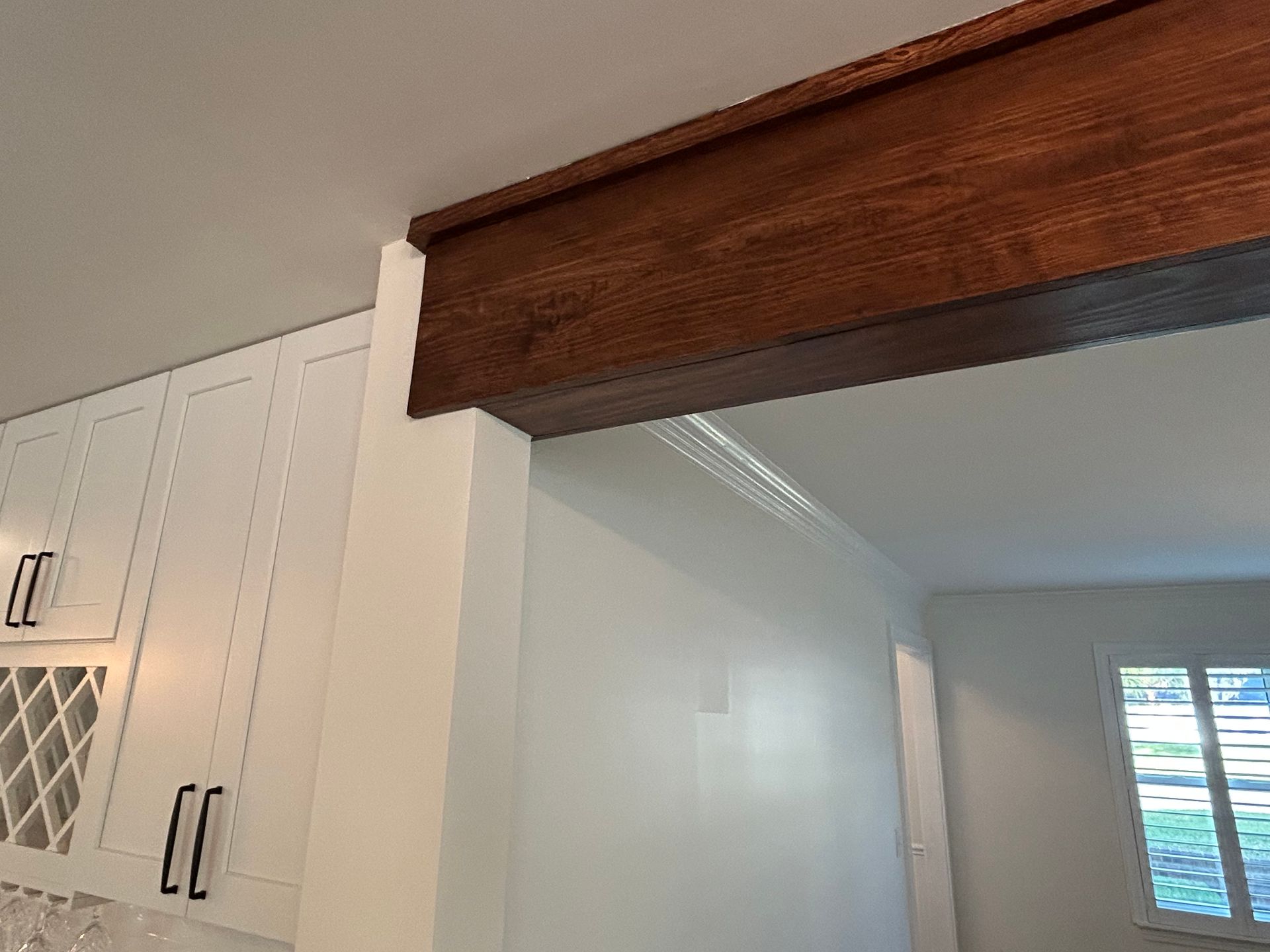 Wooden beam and white cabinets frame a doorway in a kitchen with a window visible.