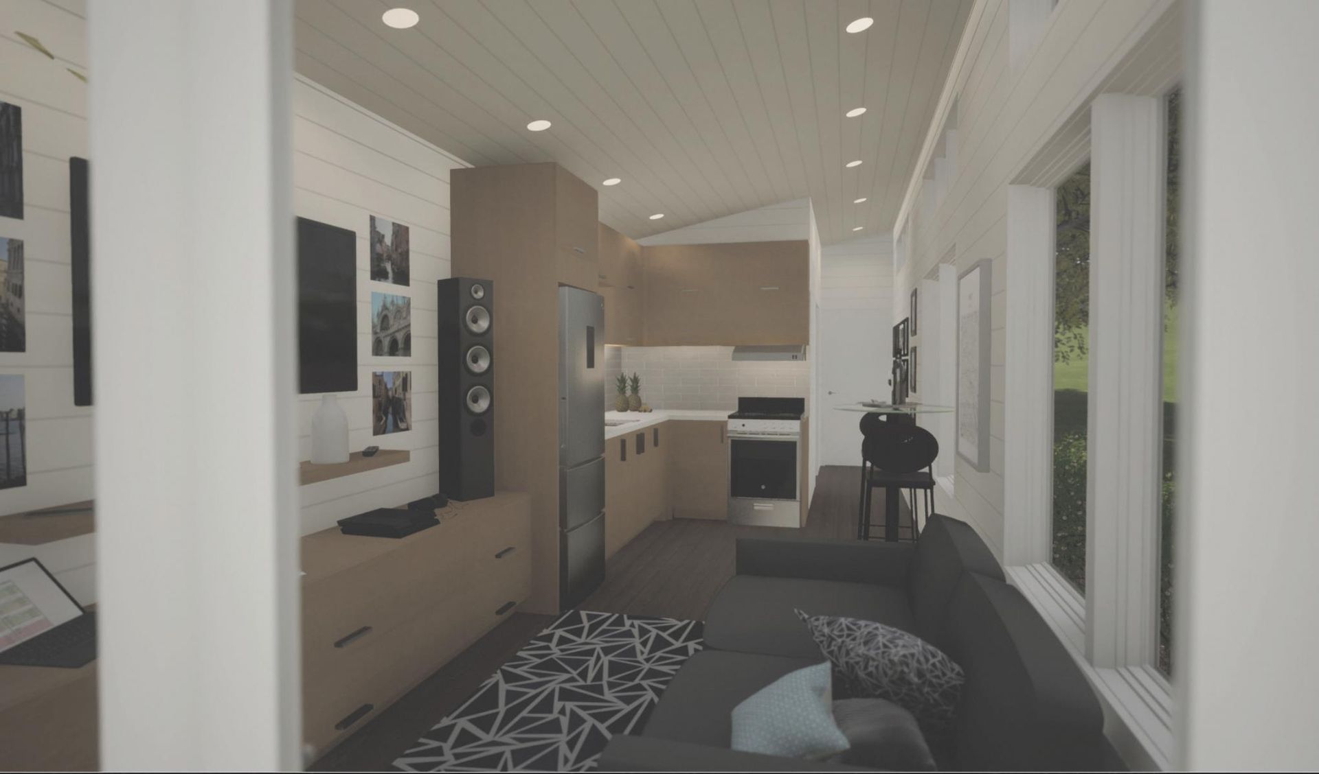 Interior view of a small, modern living space with a kitchen and seating area. Features light-colored walls, wooden cabinetry, and a dark sofa.