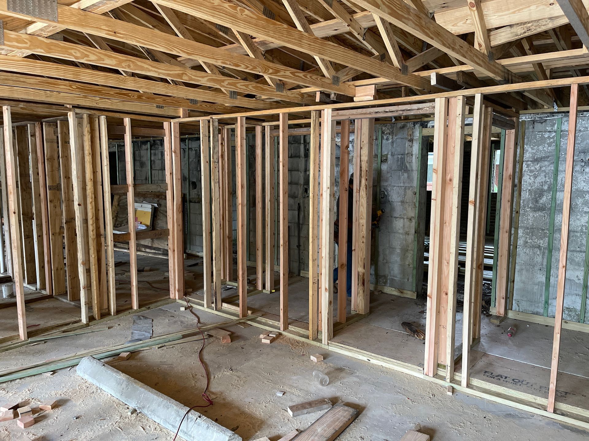 Interior view of a building under construction. Wooden studs frame walls and ceiling. Bare concrete and insulation are visible.