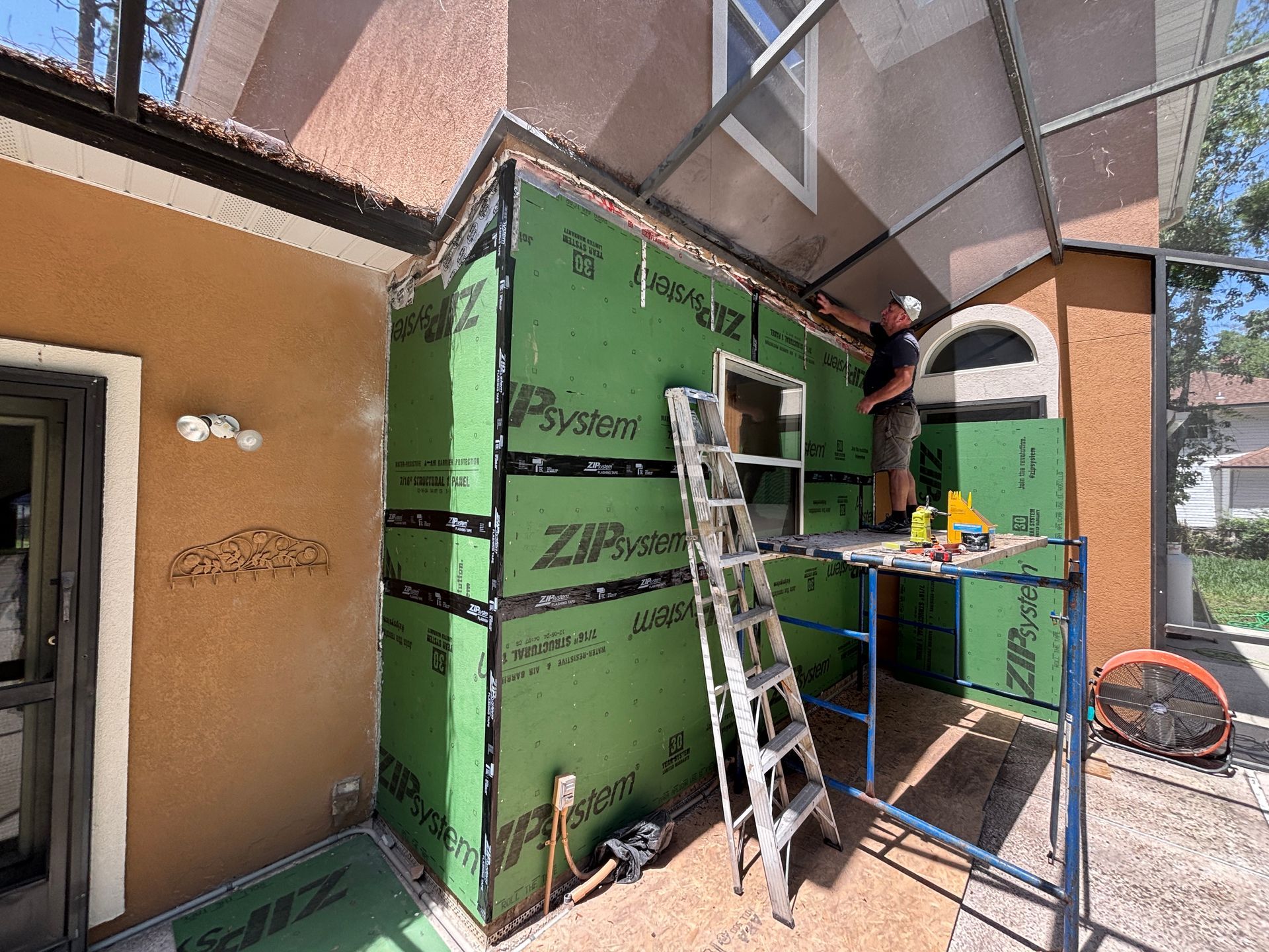 Construction worker on scaffolding attaching green building panels to the side of a building.