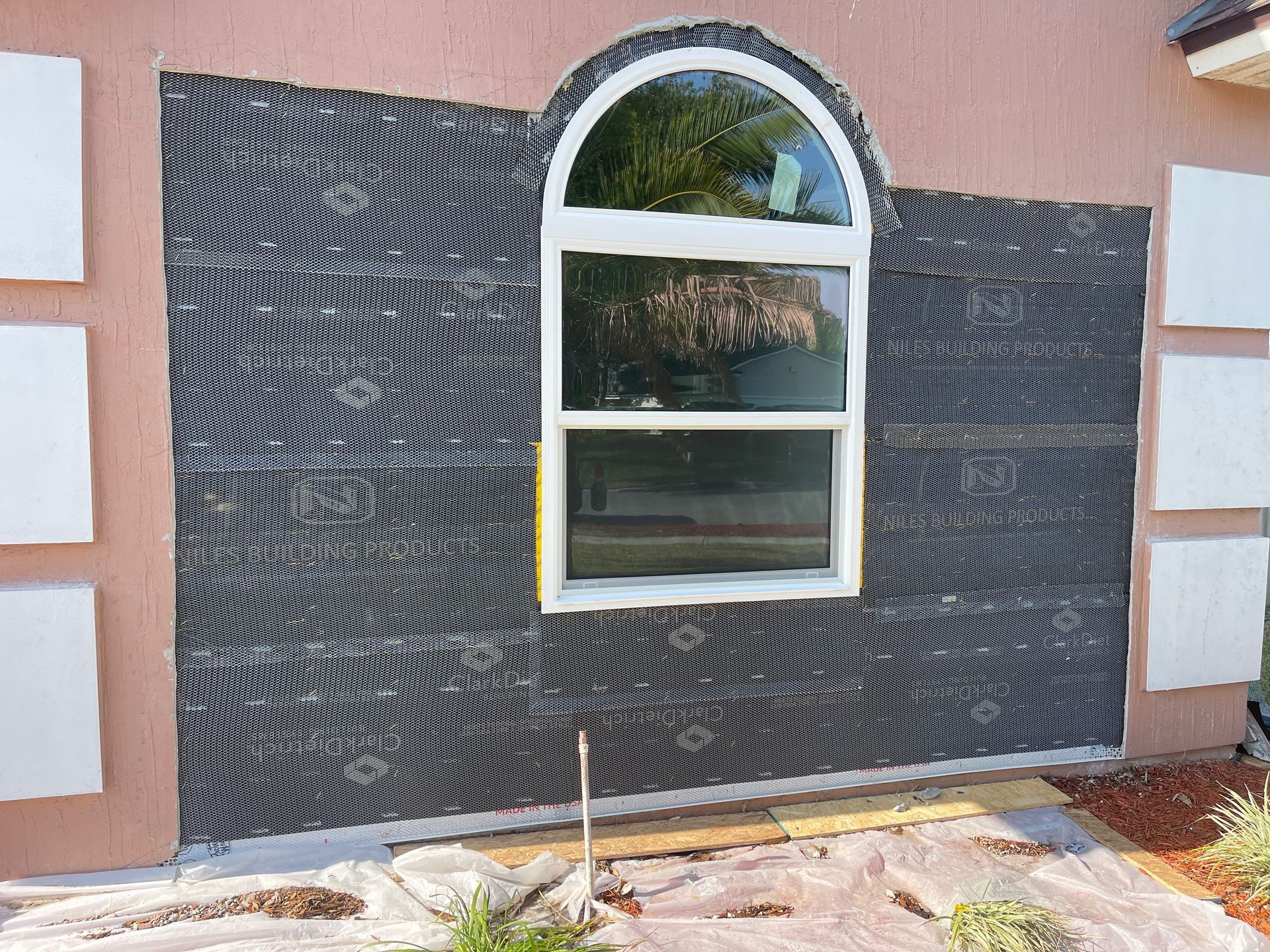 Exterior wall with an arched window; black insulation panels installed around the window, with other sections prepared for installation.