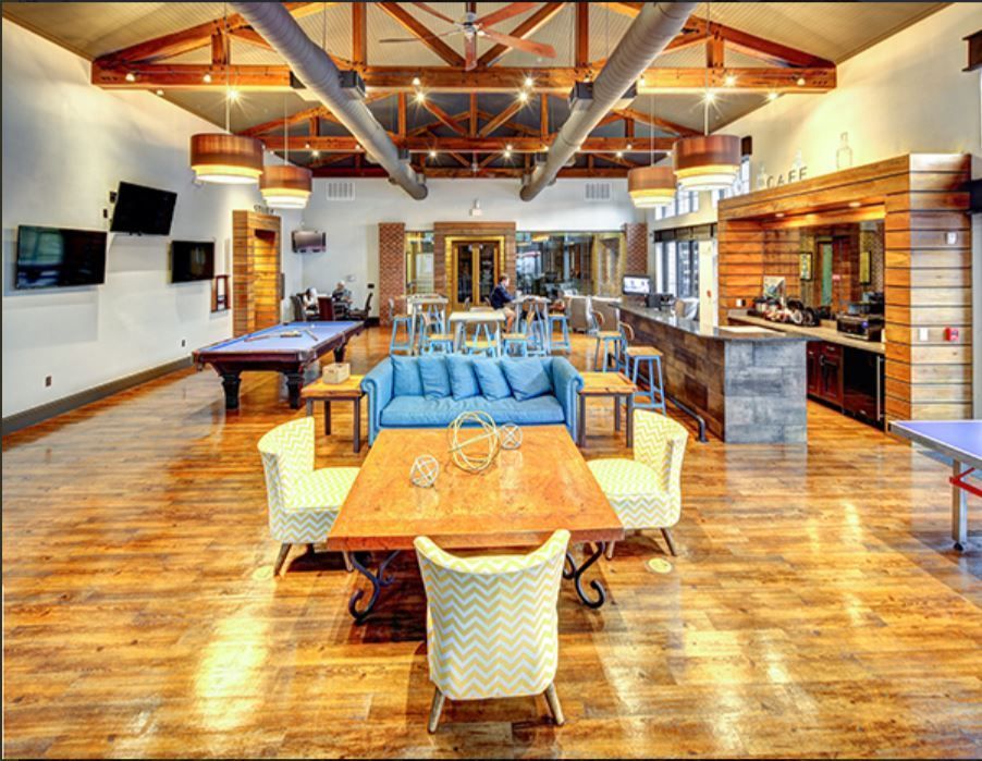Spacious lounge area with pool table, bar, and seating. Wooden floors, exposed beams, and blue couch.
