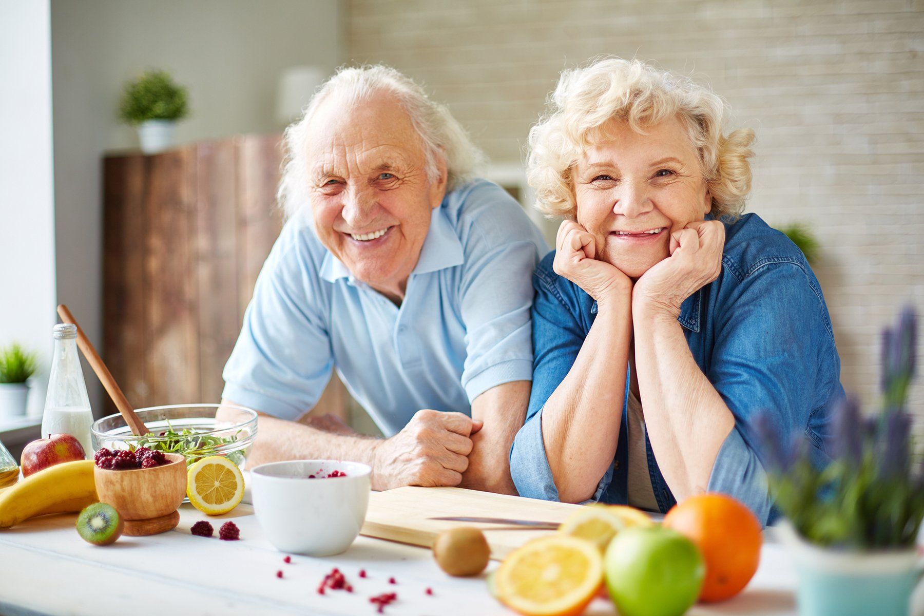 Senior couple in kitchen environment smiling at camera.