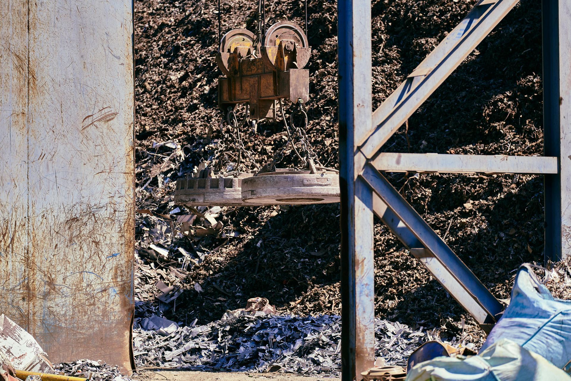 An industrial magnetic crane hovers over a large pile of scrap metal in a recycling facility.