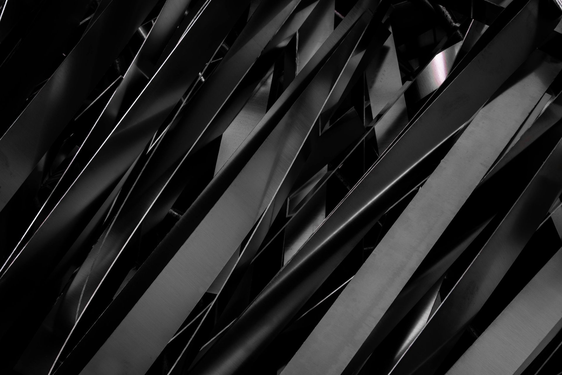 A black and white abstract close-up of overlapping, angled strips of dark material, creating a pattern of geometric lines.