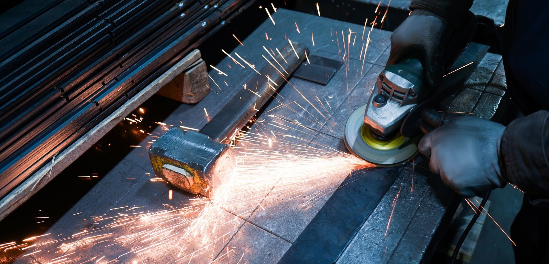A gloved person uses an angle grinder to cut or smooth a piece of metal, creating a spray of bright sparks.