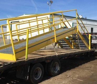 A yellow metal staircase with handrails loaded onto a flatbed trailer in an outdoor yard.