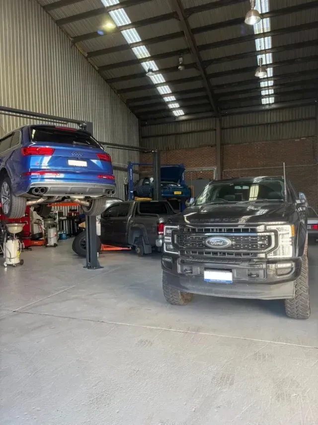 A Garage Interior with A Black Ford Pickup and A Blue SUV on A Lift  — Level Up Automotive In Unanderra, NSW