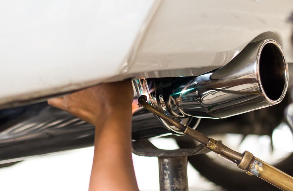 A Person Welding a Chrome Exhaust Pipe to A Car — Level Up Automotive In Unanderra, NSW