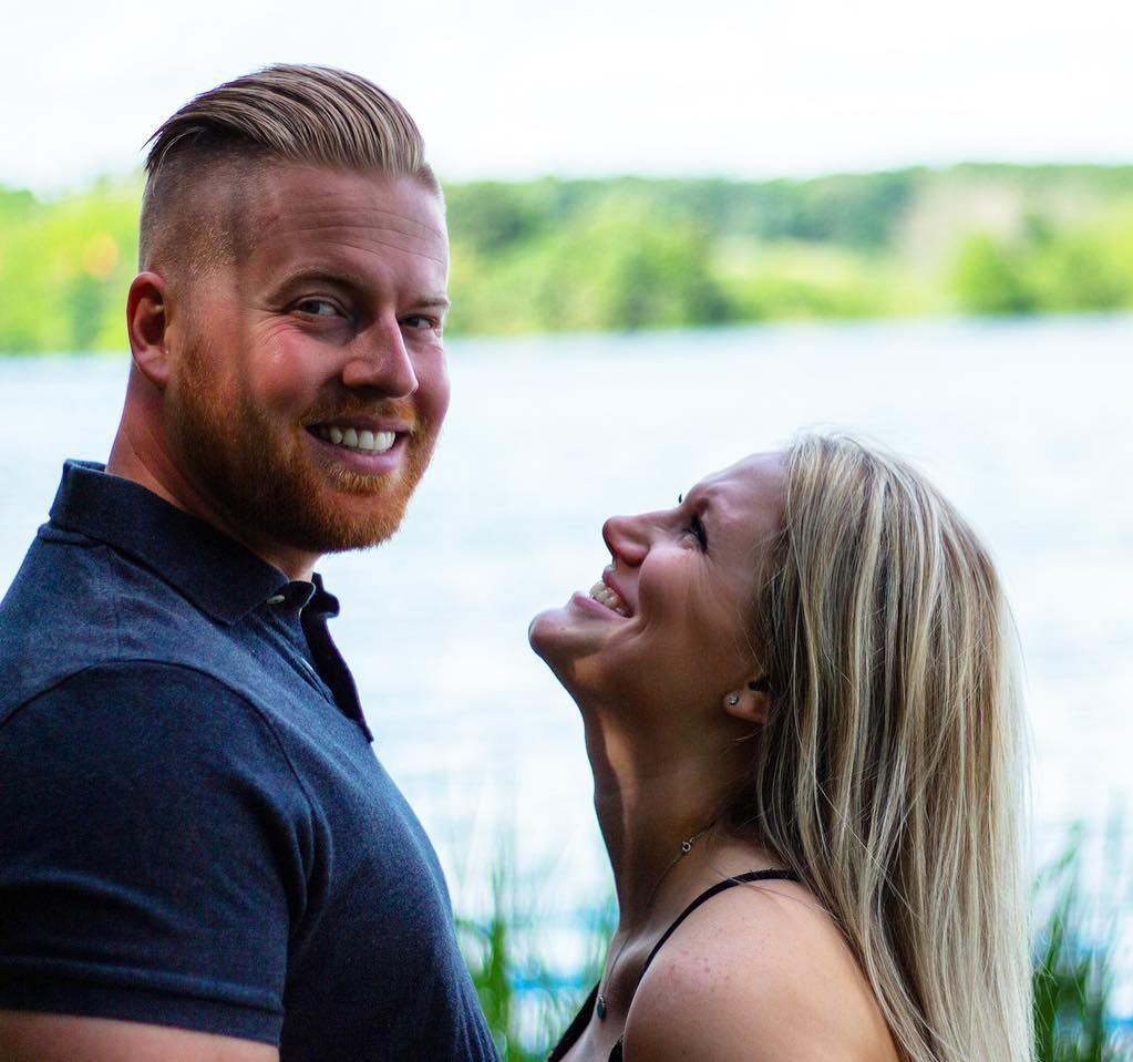 Man smiling at camera, woman looking up laughing, near a lake.
