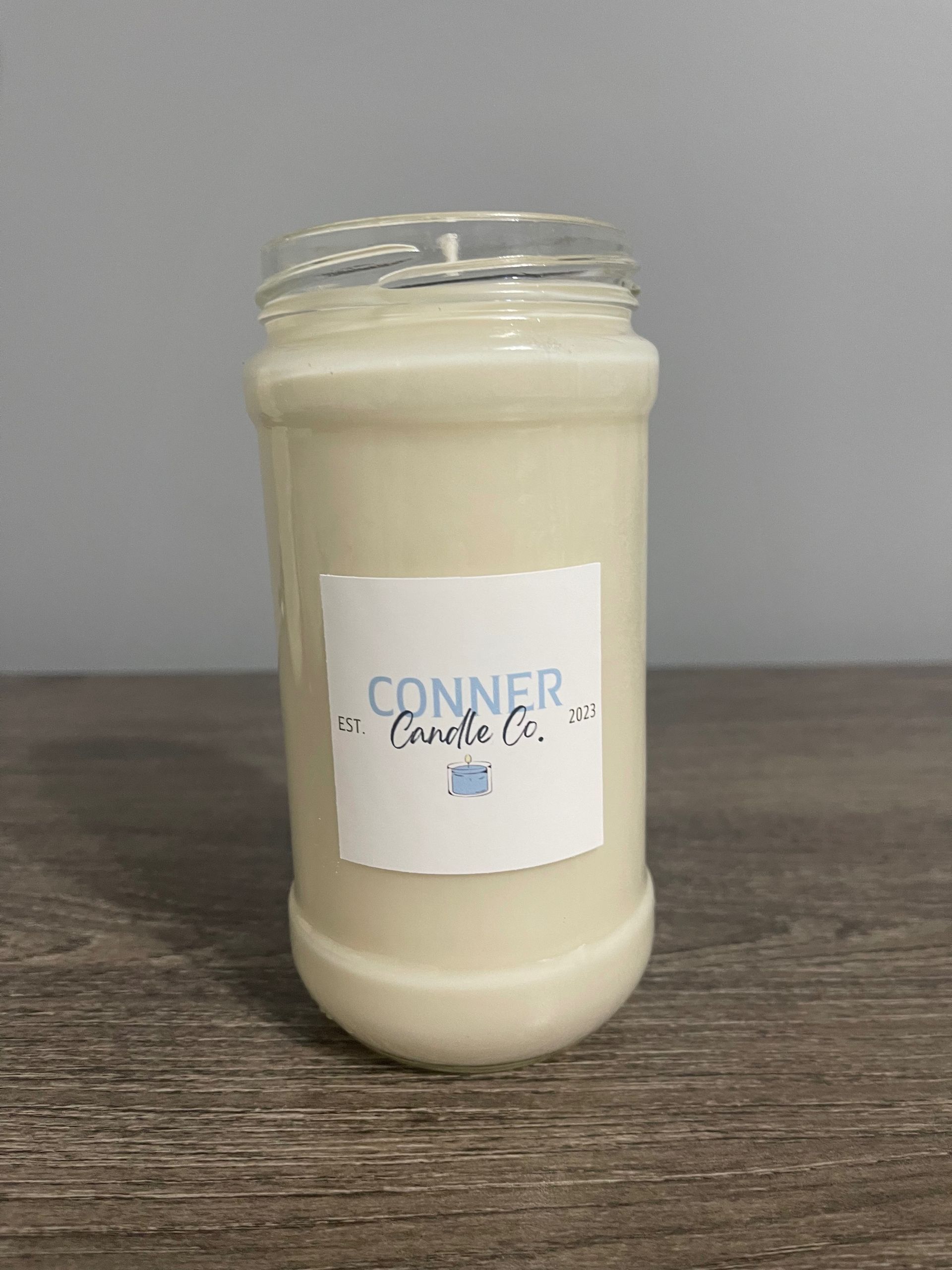 A white candle in a clear jar with a white label that reads 