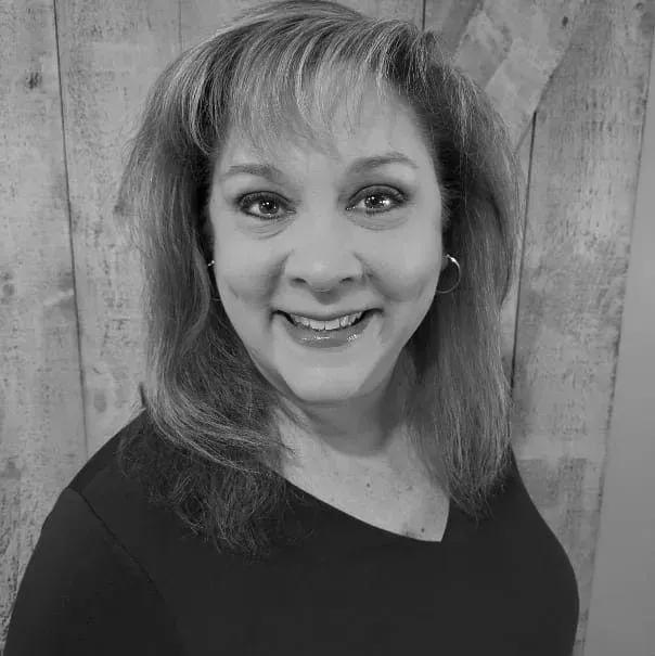 Woman with light-colored hair smiles at the camera in front of a wooden wall.