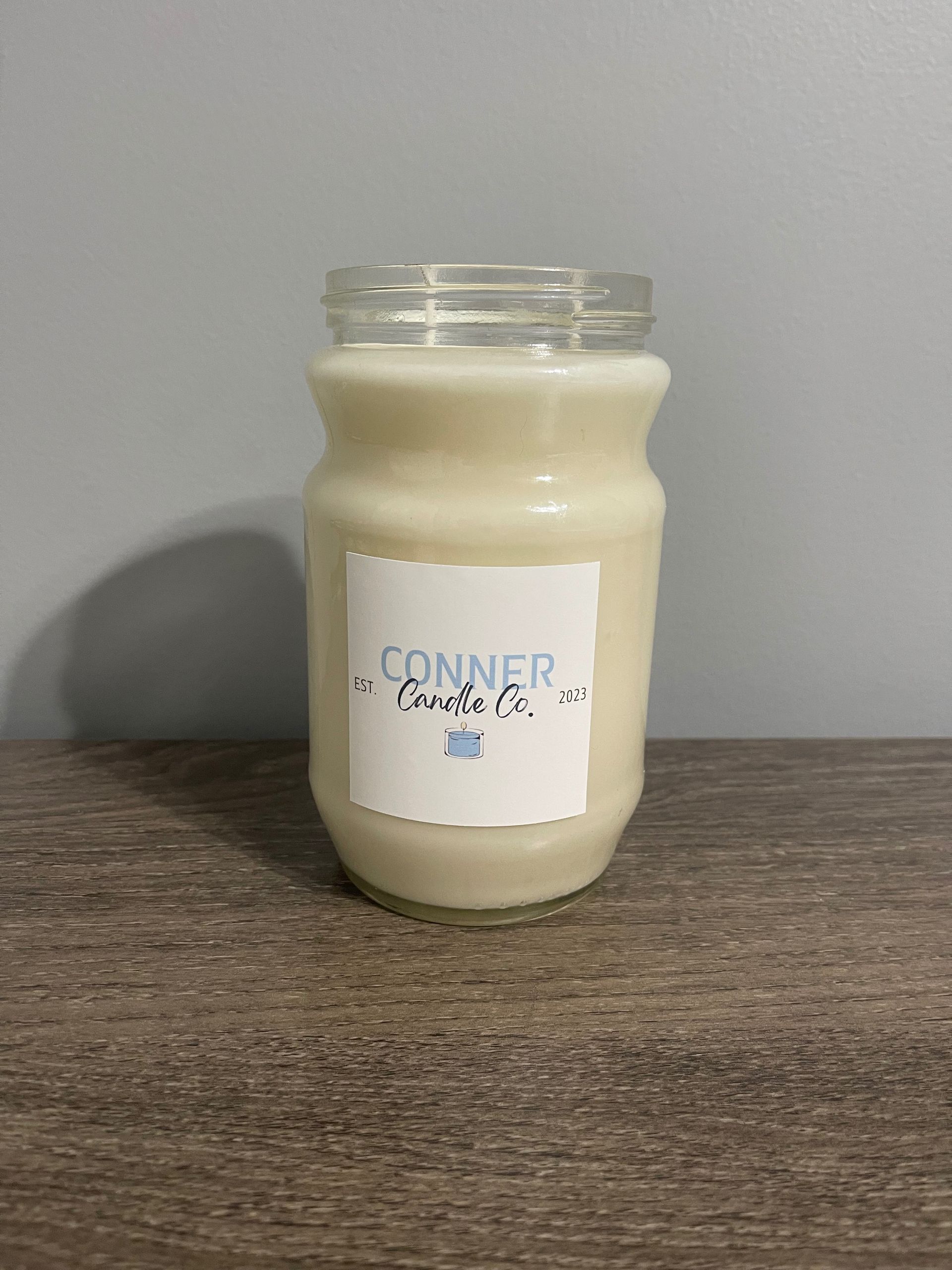 Glass jar candle with cream wax, on a wood surface, label says 