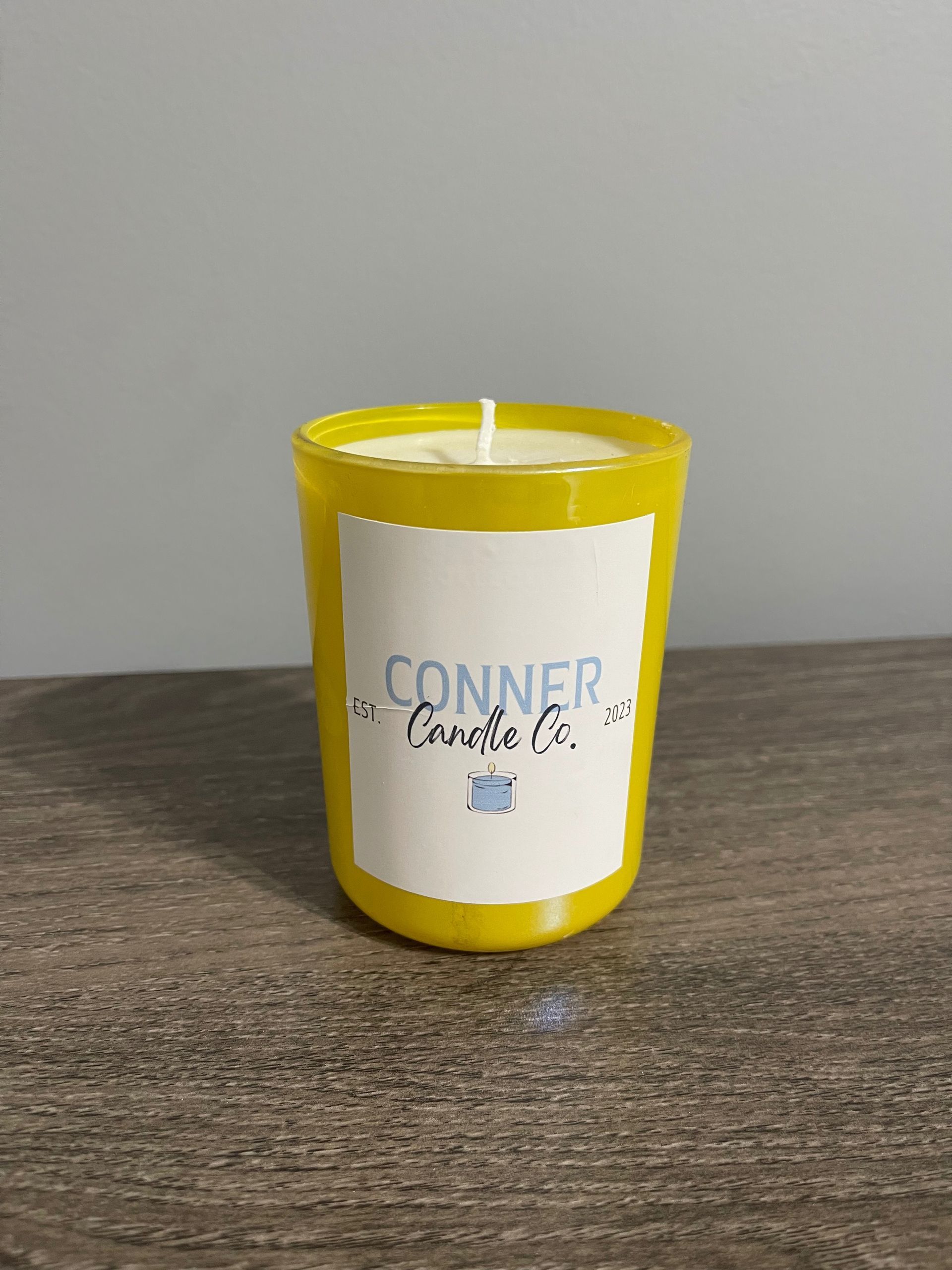 Yellow votive candle in a glass holder with a white label reading 