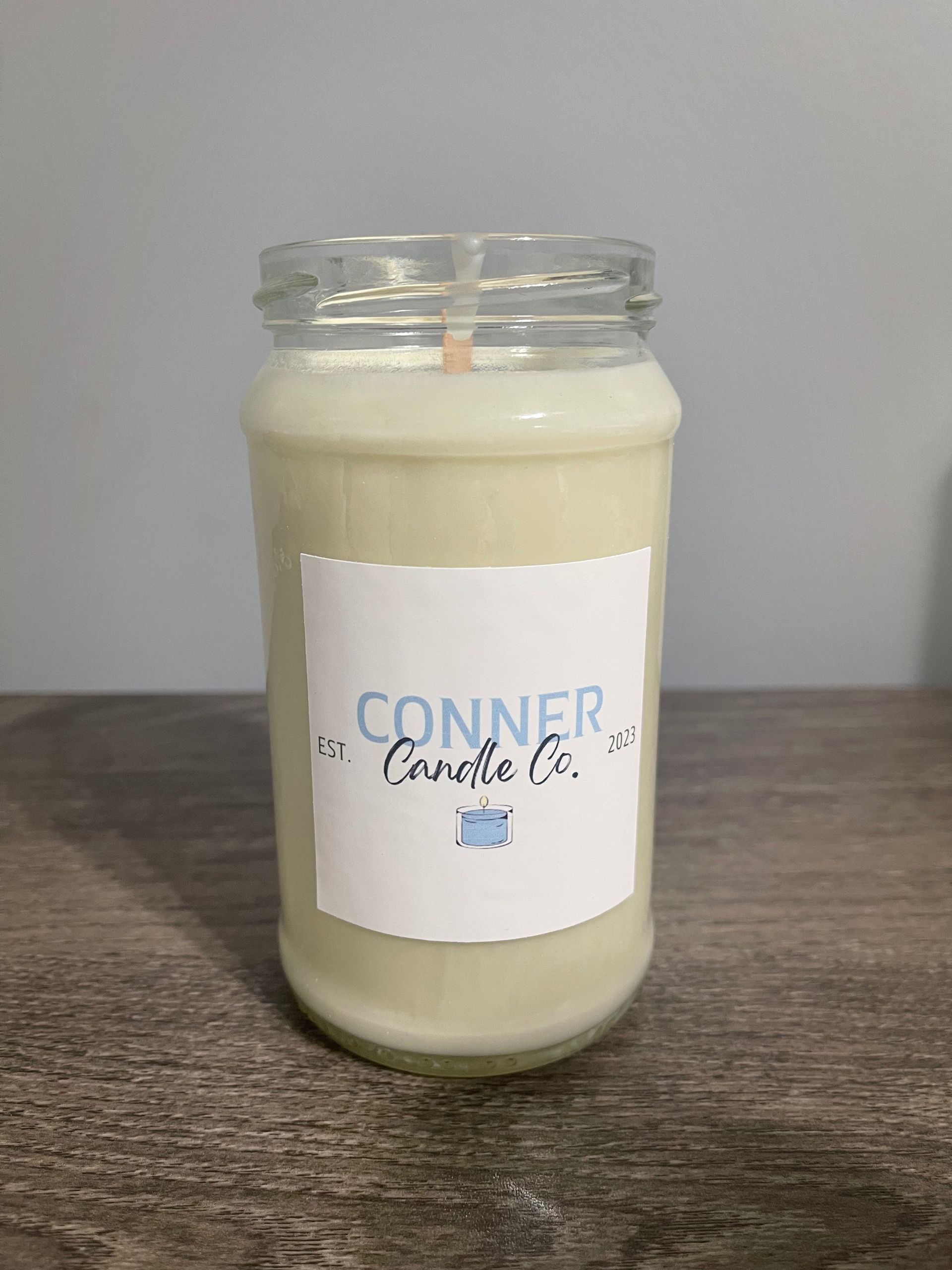 Candle in a glass jar with a white label, on a wooden surface.