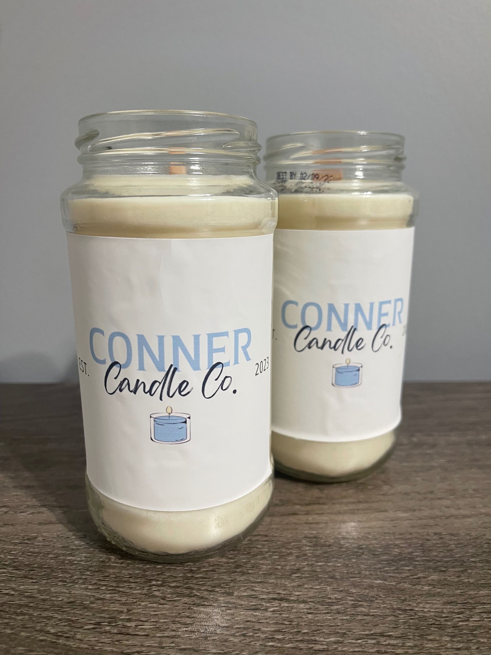 Two glass jar candles with white wax and blue and white labels that read 