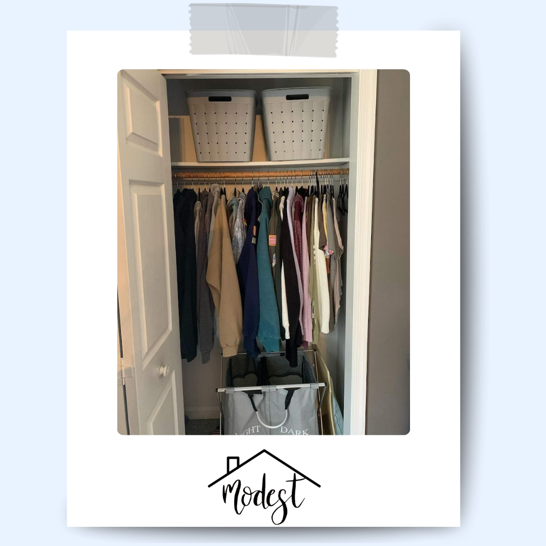 Closet with clothes hanging on a rod, two storage bins on top shelf, and a laundry hamper below.