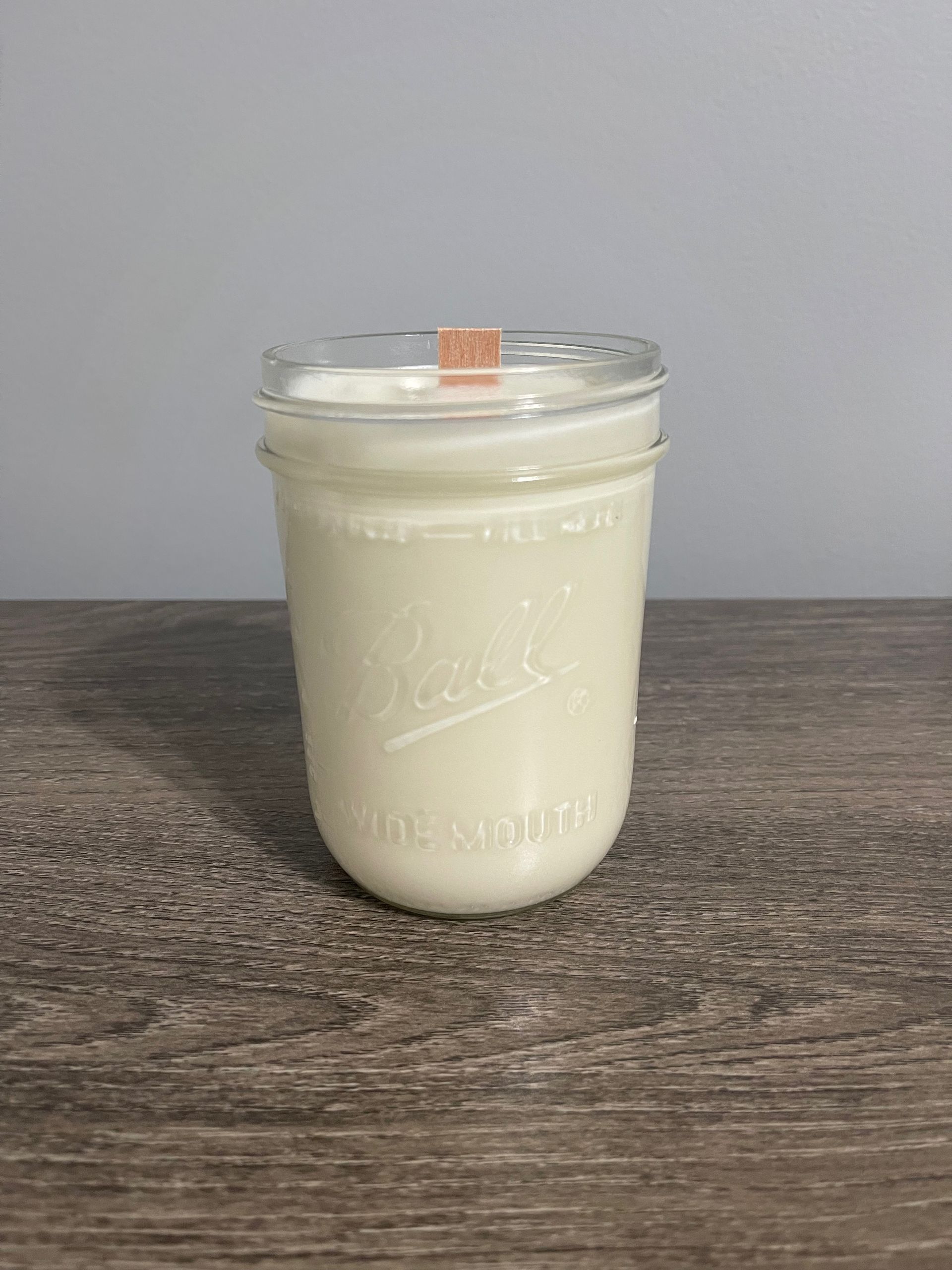 White candle in a glass mason jar on a wooden surface.