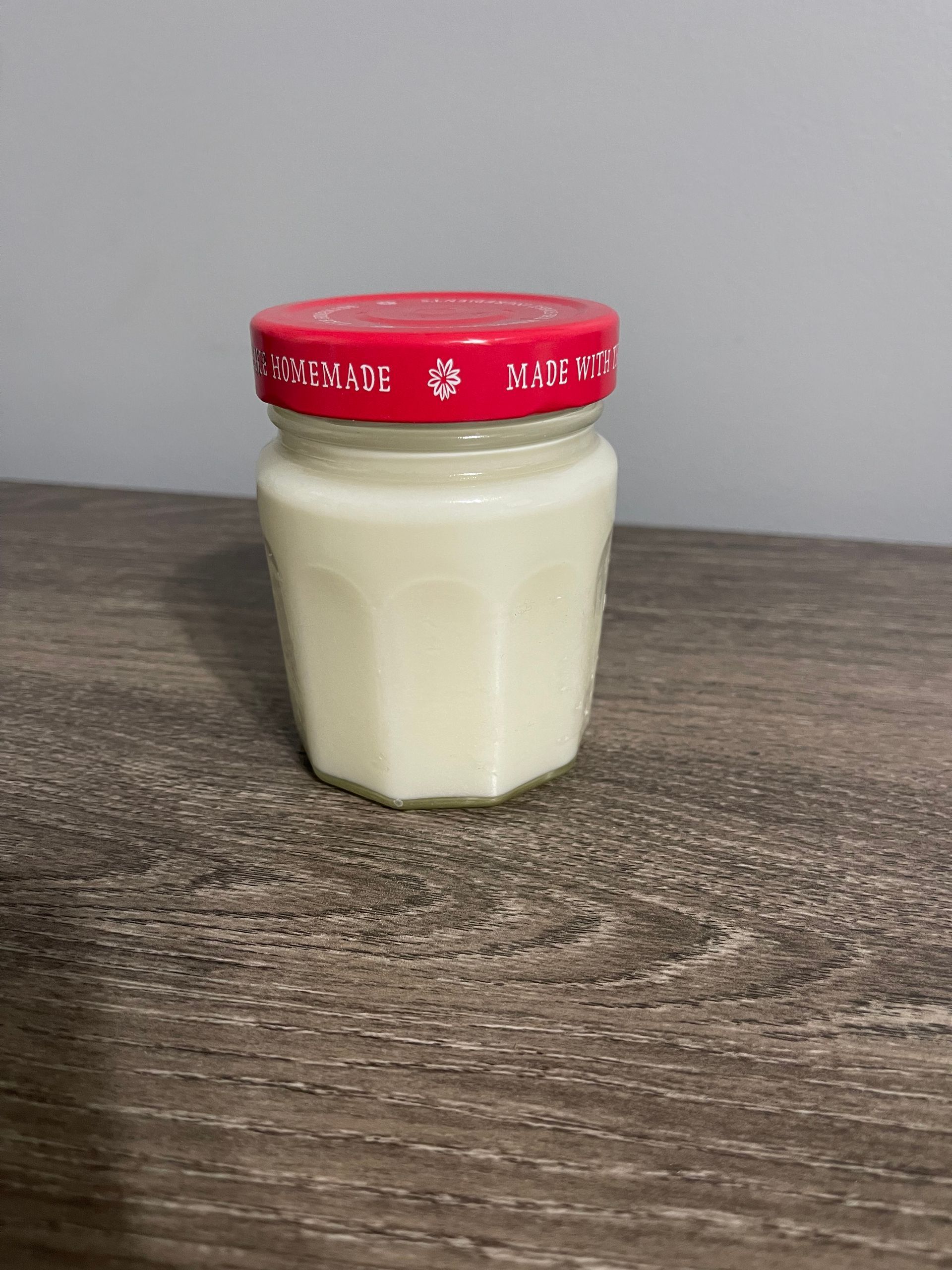 Jar of opaque white cream with a red lid on a wood-grain surface.