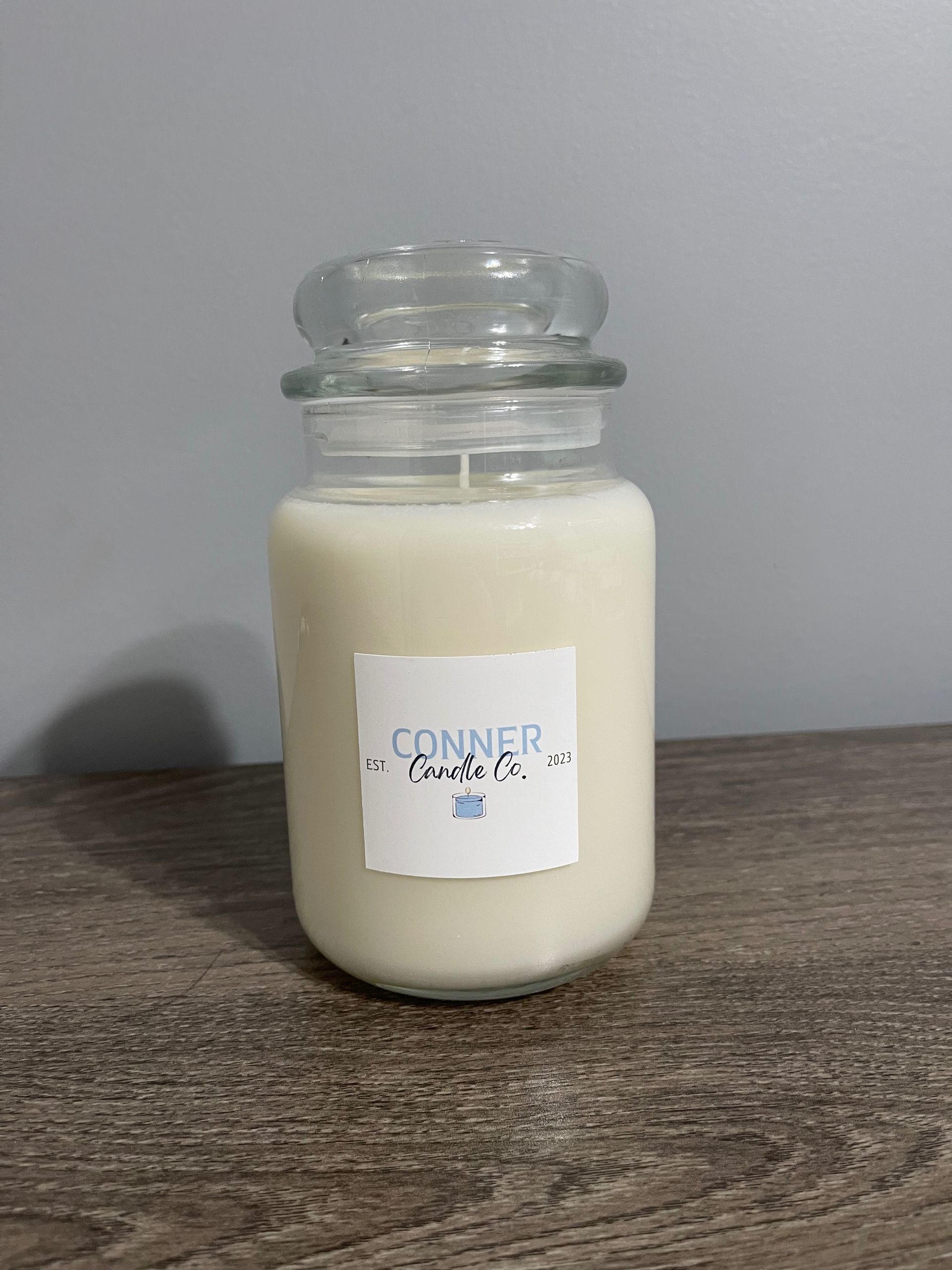 White candle in a clear jar with a lid; a label reads 