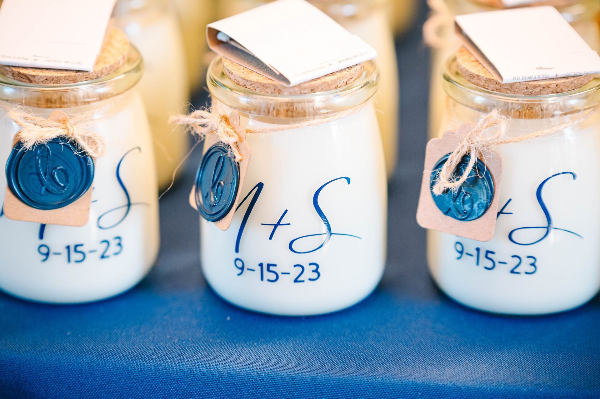 Glass jars with creamy contents, initials, date, and blue wax seals on a blue tablecloth.