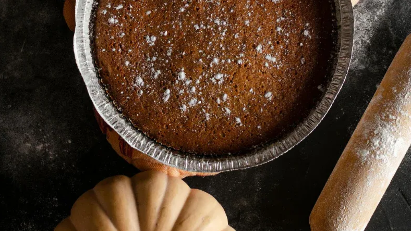 Pumpkin pie in foil pan, dusted with powder, beside a rolling pin and pumpkins.