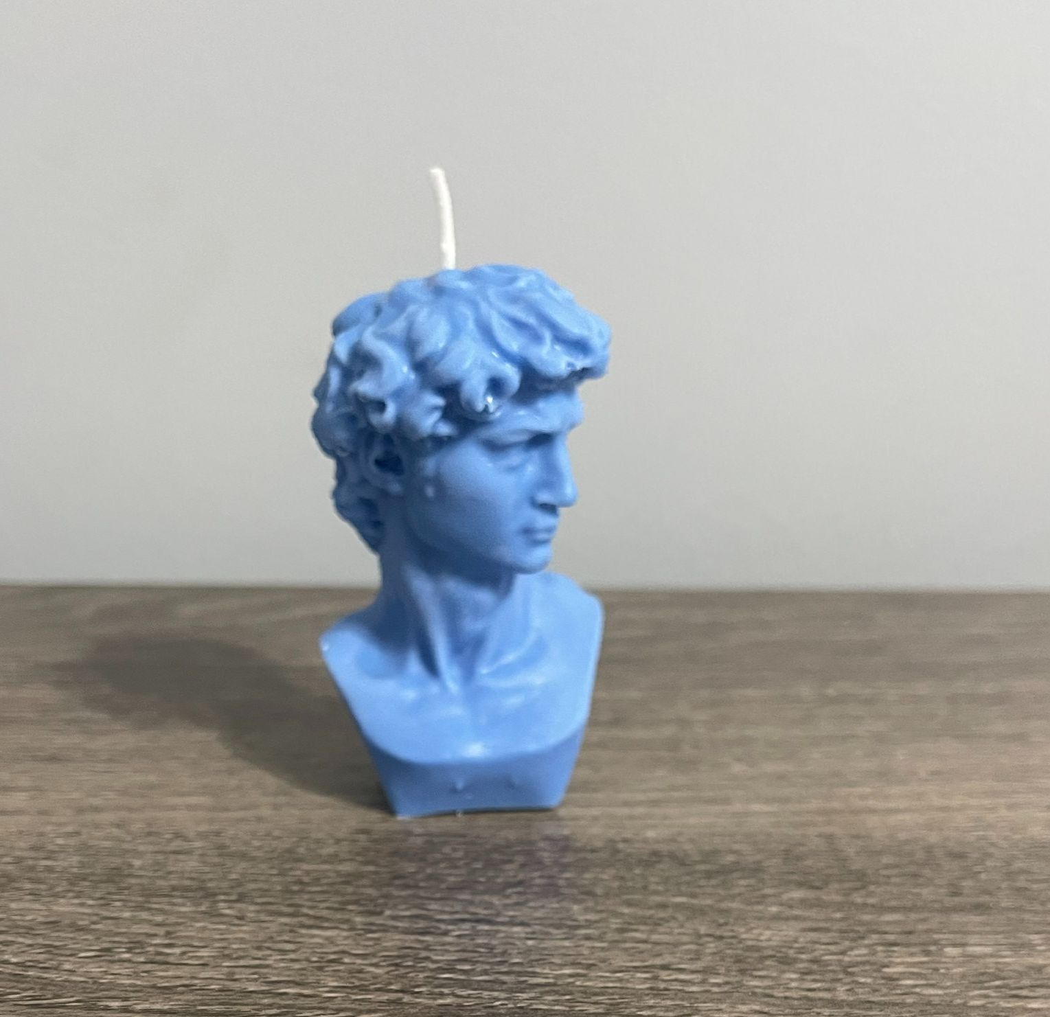 Blue candle shaped like a bust of the statue David, on a wooden surface.