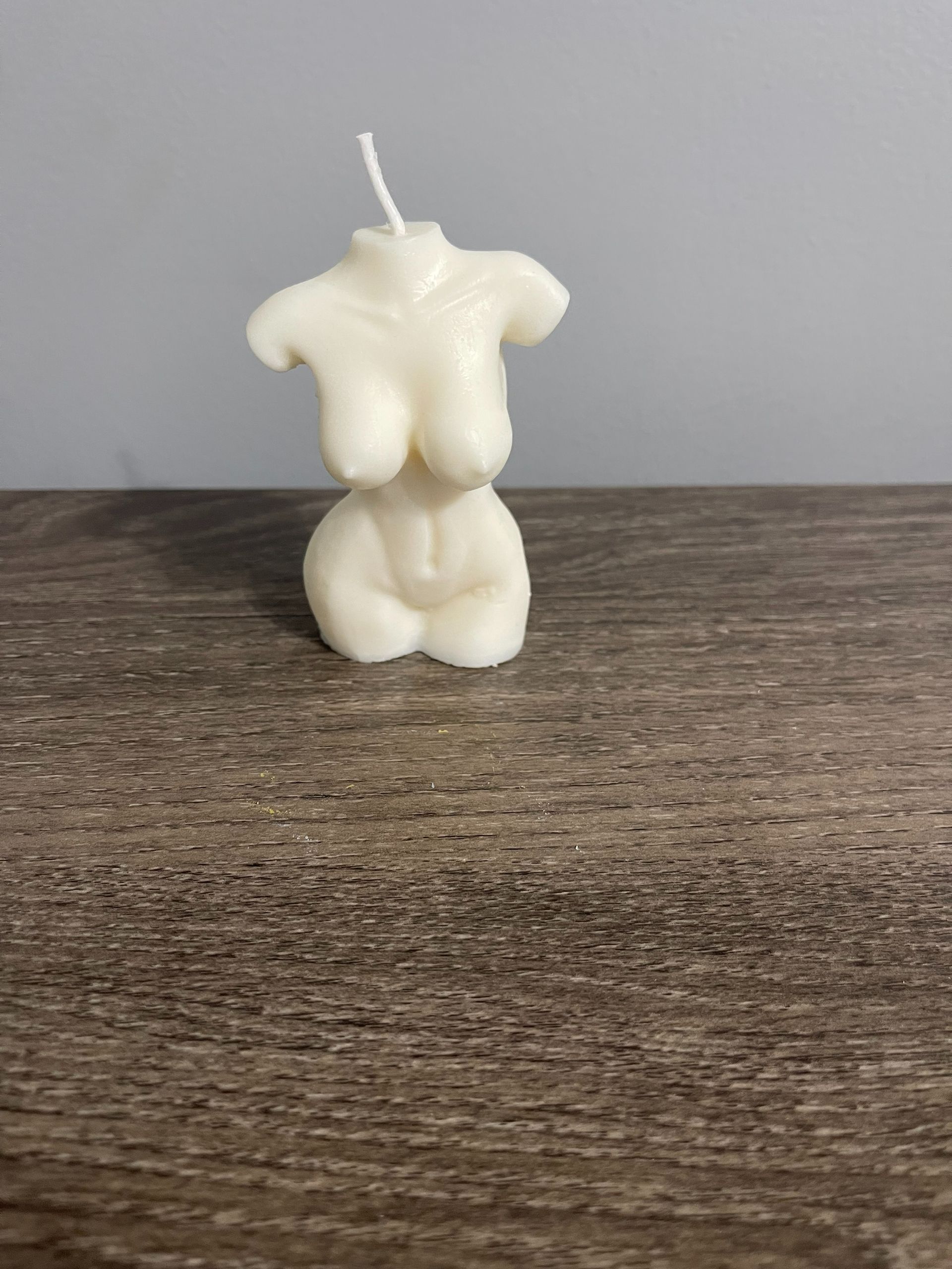 Cream-colored, torso-shaped candle with a wick, sitting on a wooden surface.