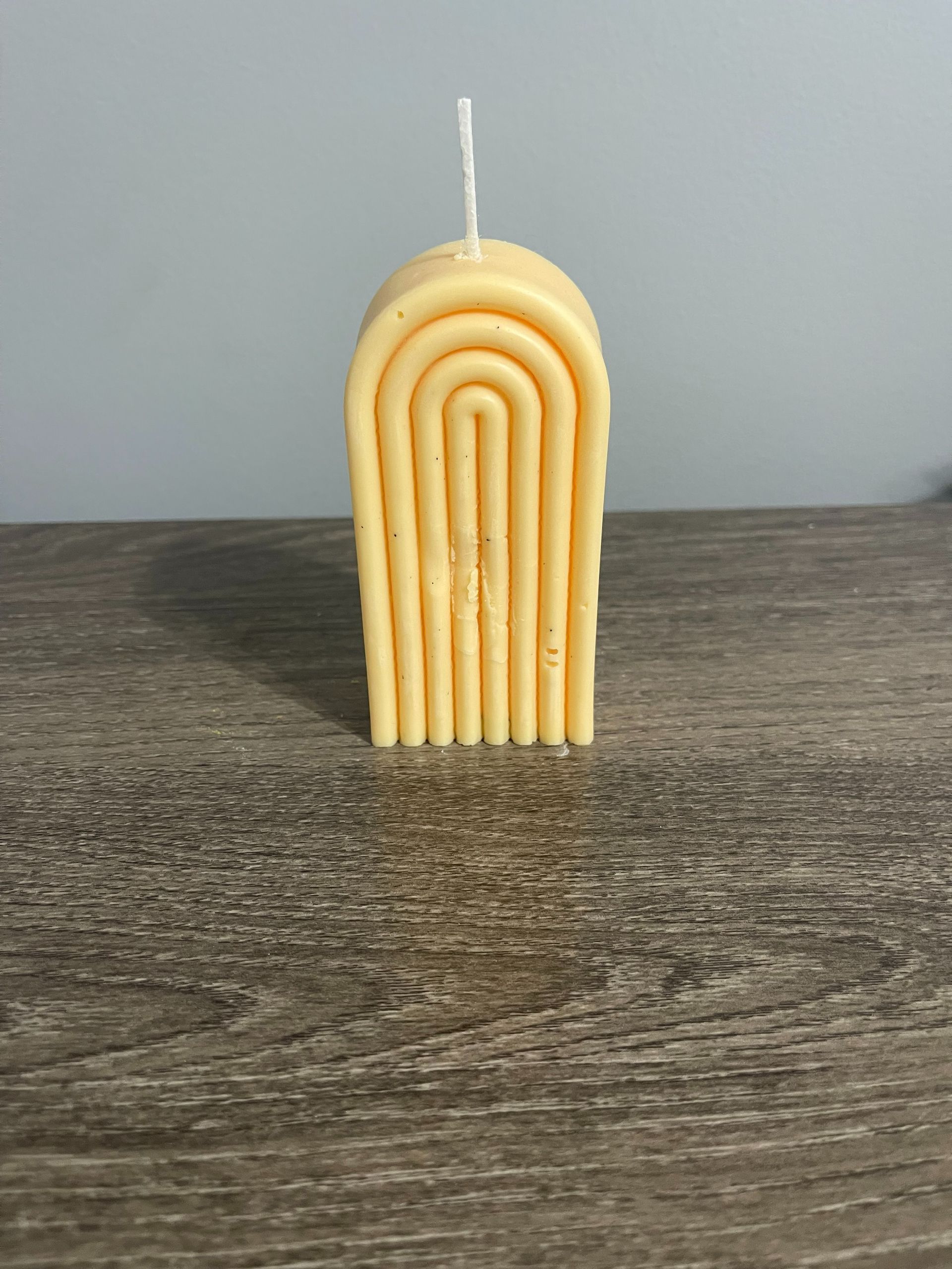 Yellow candle in a curved, arch design on a wooden surface.