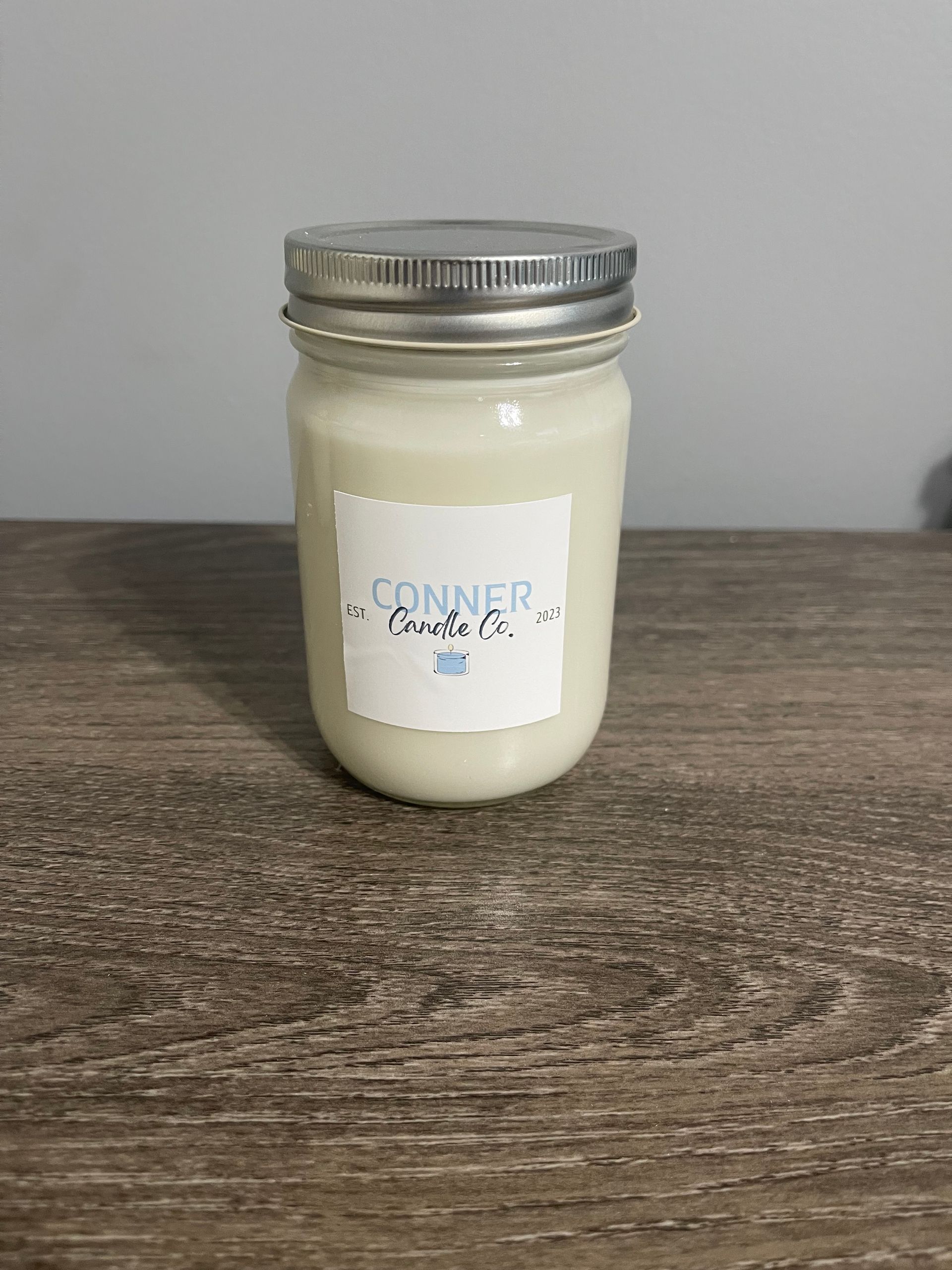 White candle in a glass jar with a silver lid, labeled 