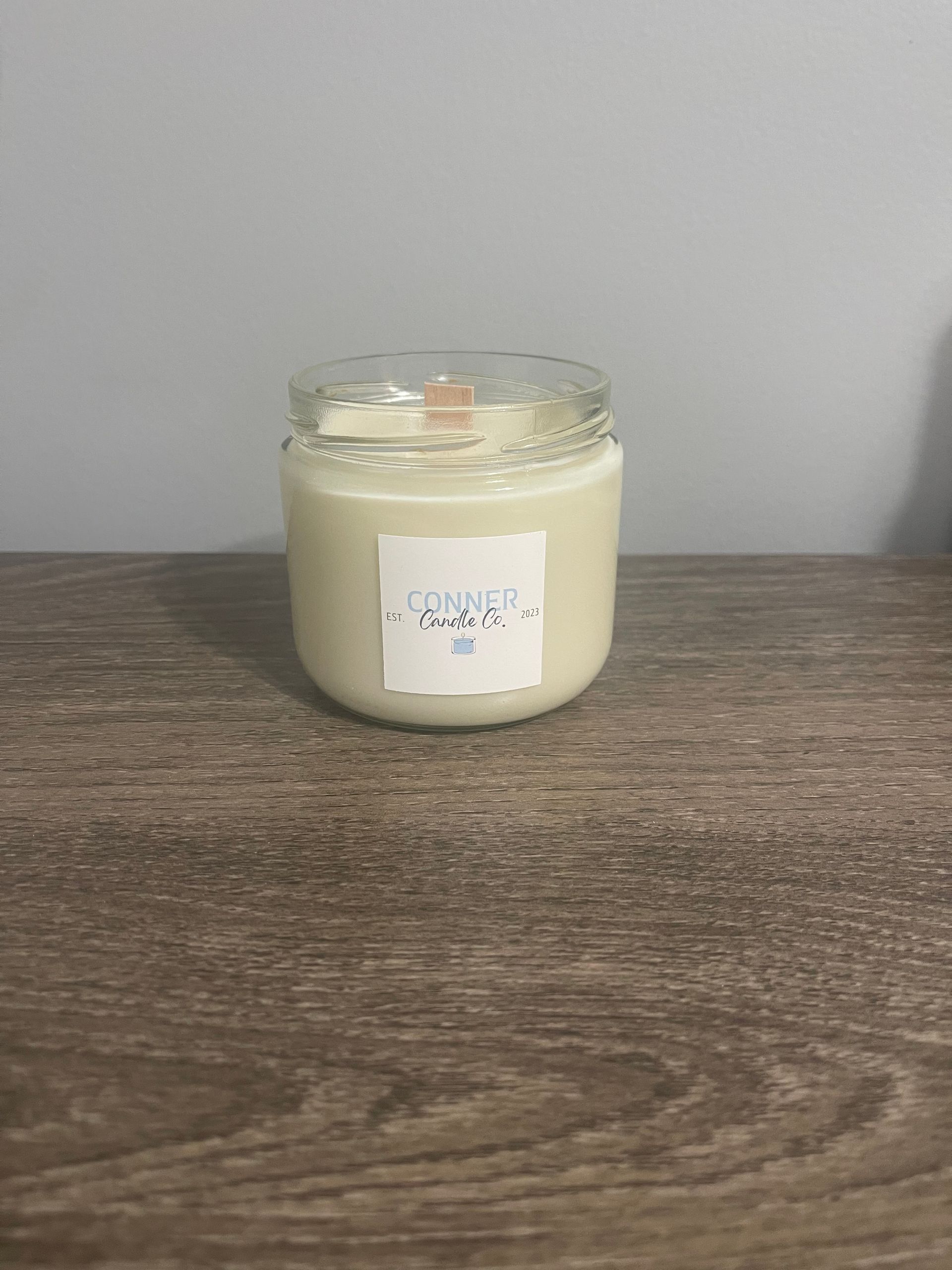 Candle in a clear glass jar on a wooden surface. Label visible.