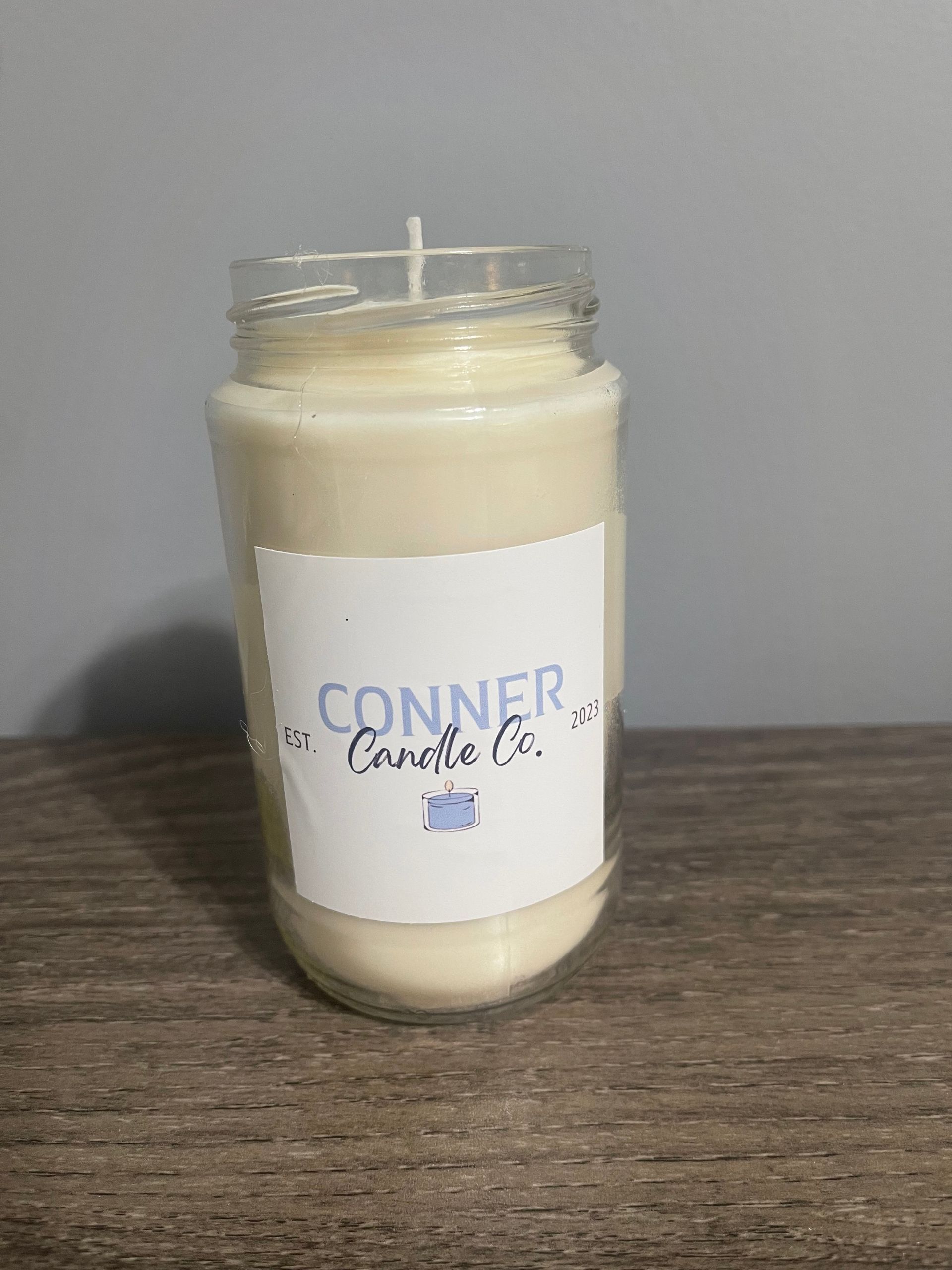 Cream-colored candle in a clear glass jar with a white label reading 
