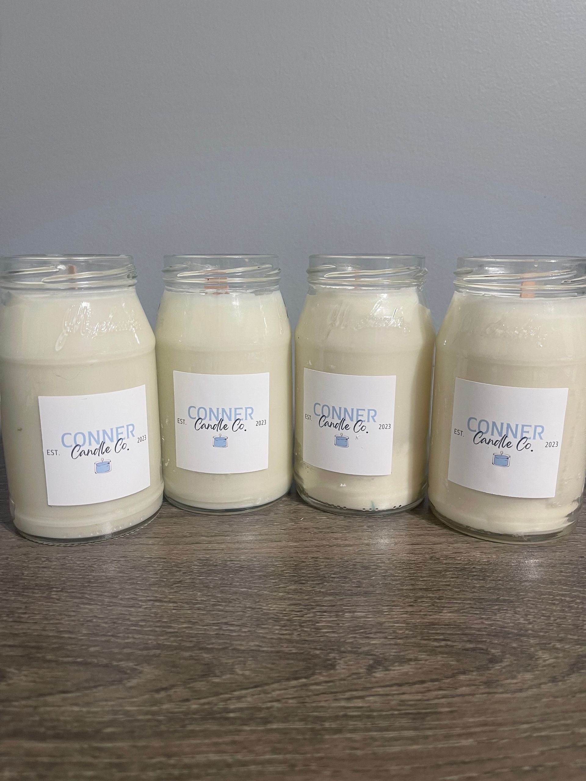 Candle in a clear glass jar on a wooden surface, with a label that says 