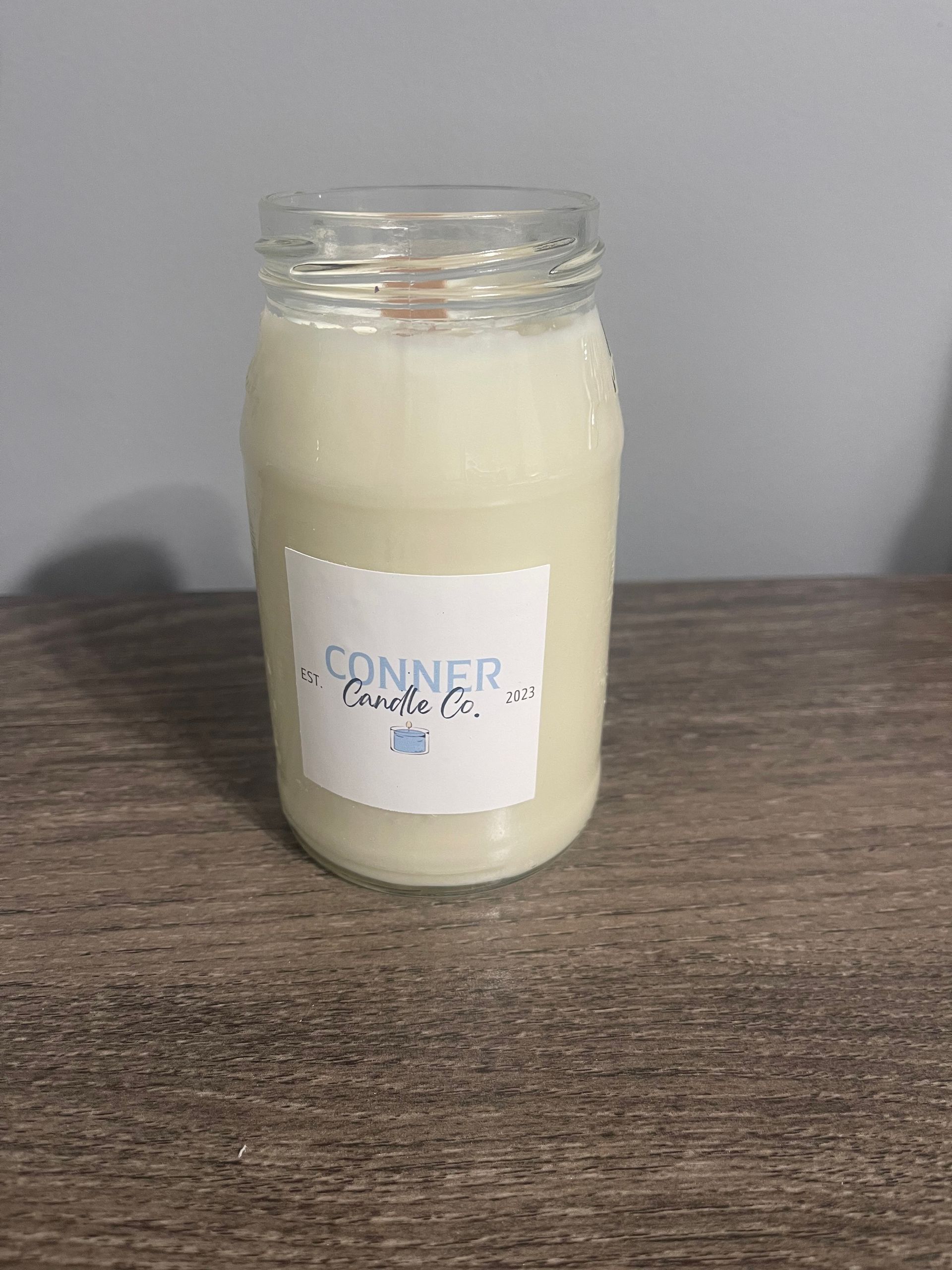 Candle in a clear glass jar on a wooden surface, with a label that says 