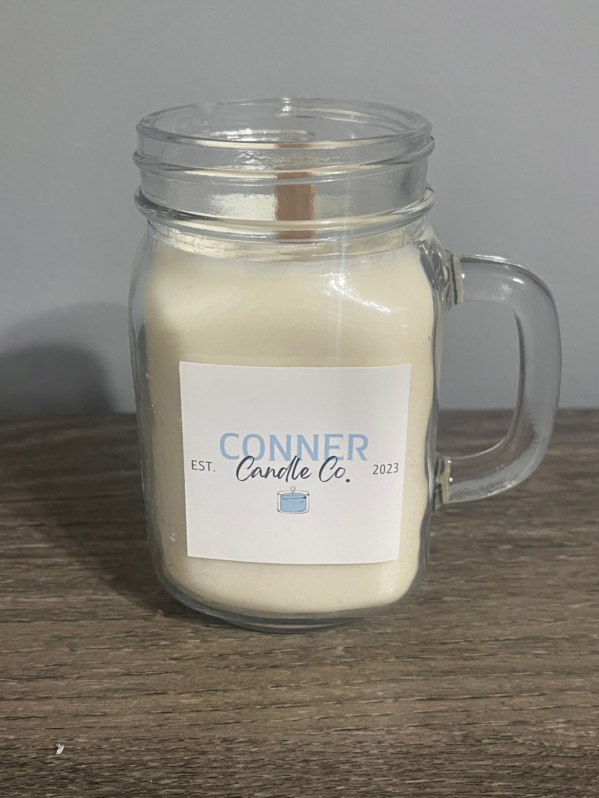 Cream-colored candle in a mason jar mug with wooden wick and label that reads 