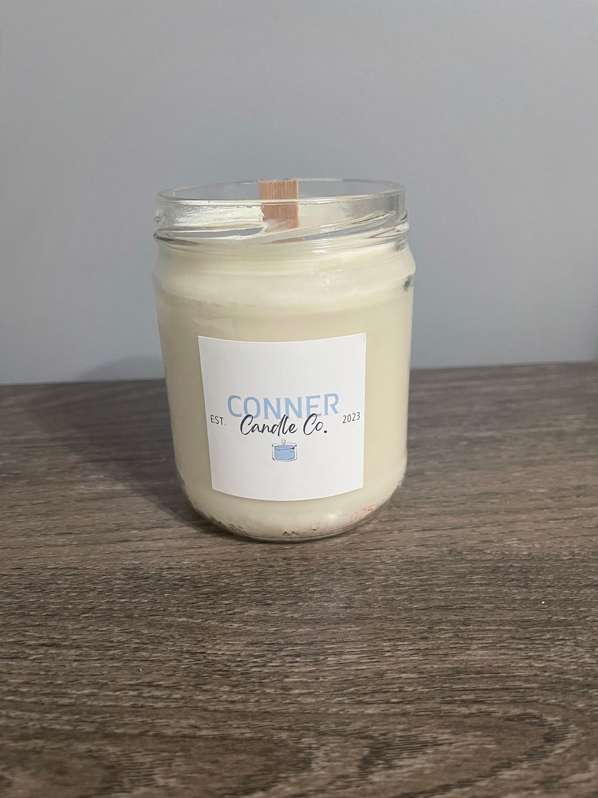 A white candle in a glass jar with a label that says 
