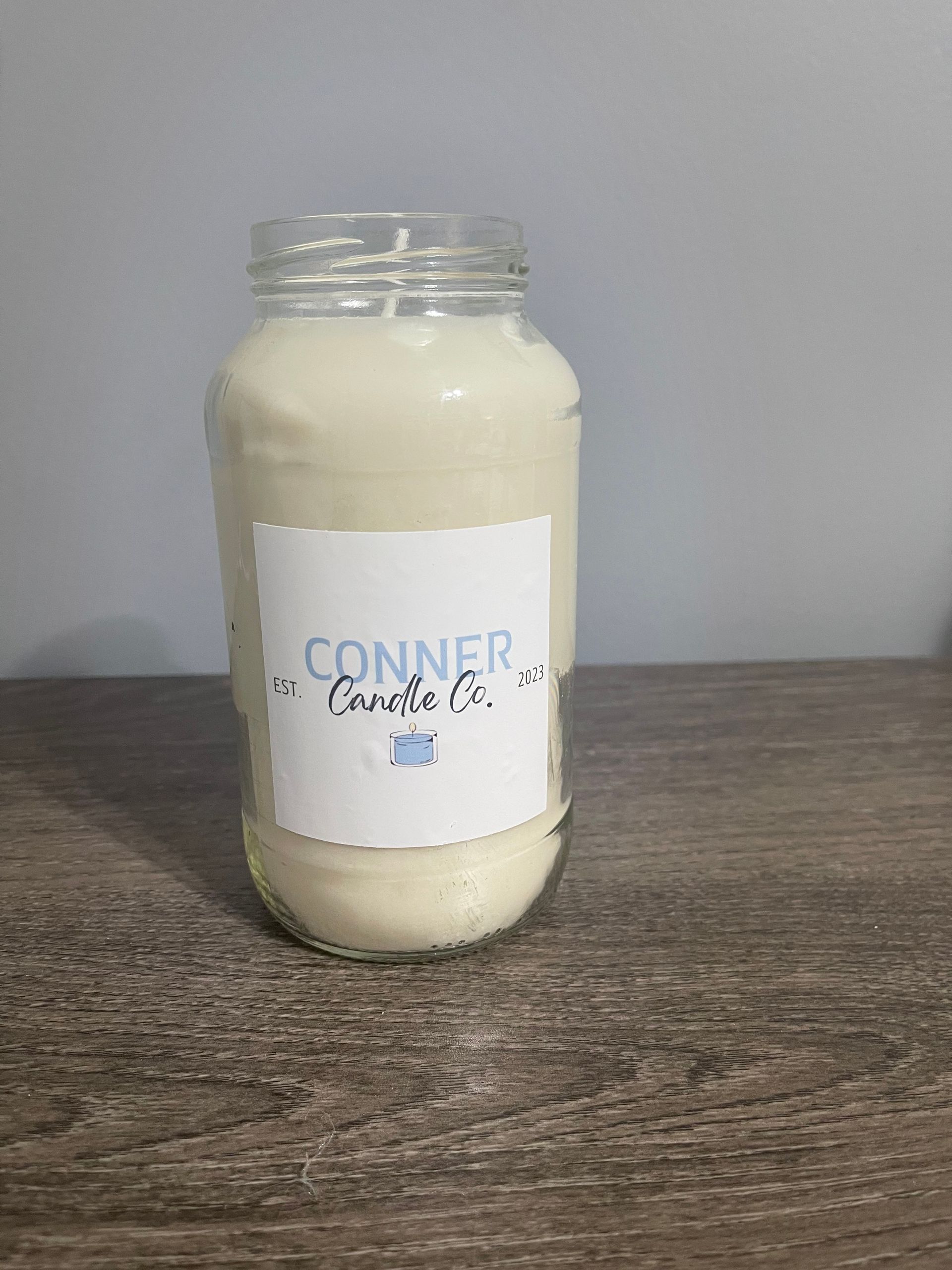 White candle in a glass jar, with a blue and white label that reads 