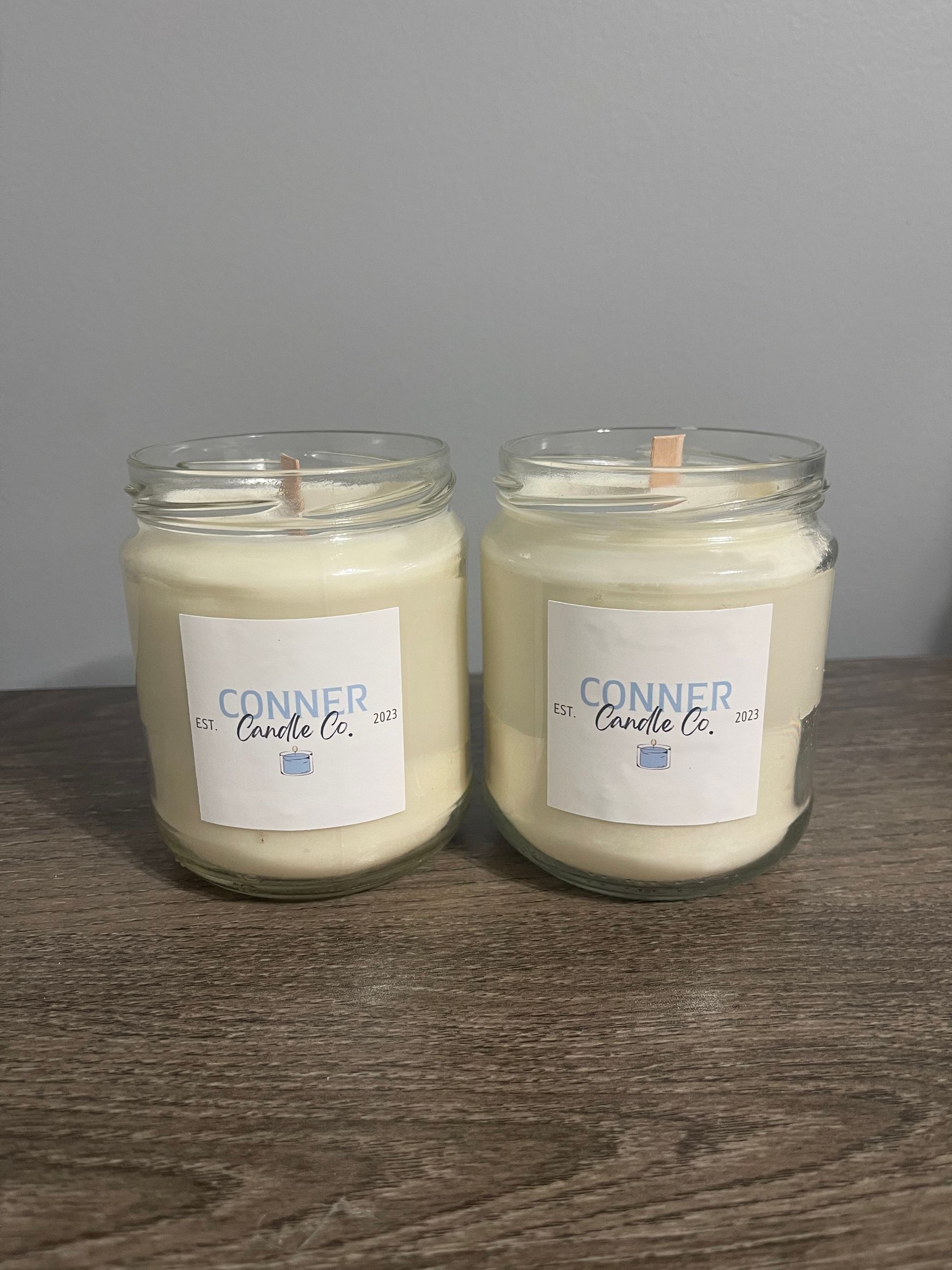 Two glass jar candles with white wax and labels, sitting on a wooden surface.