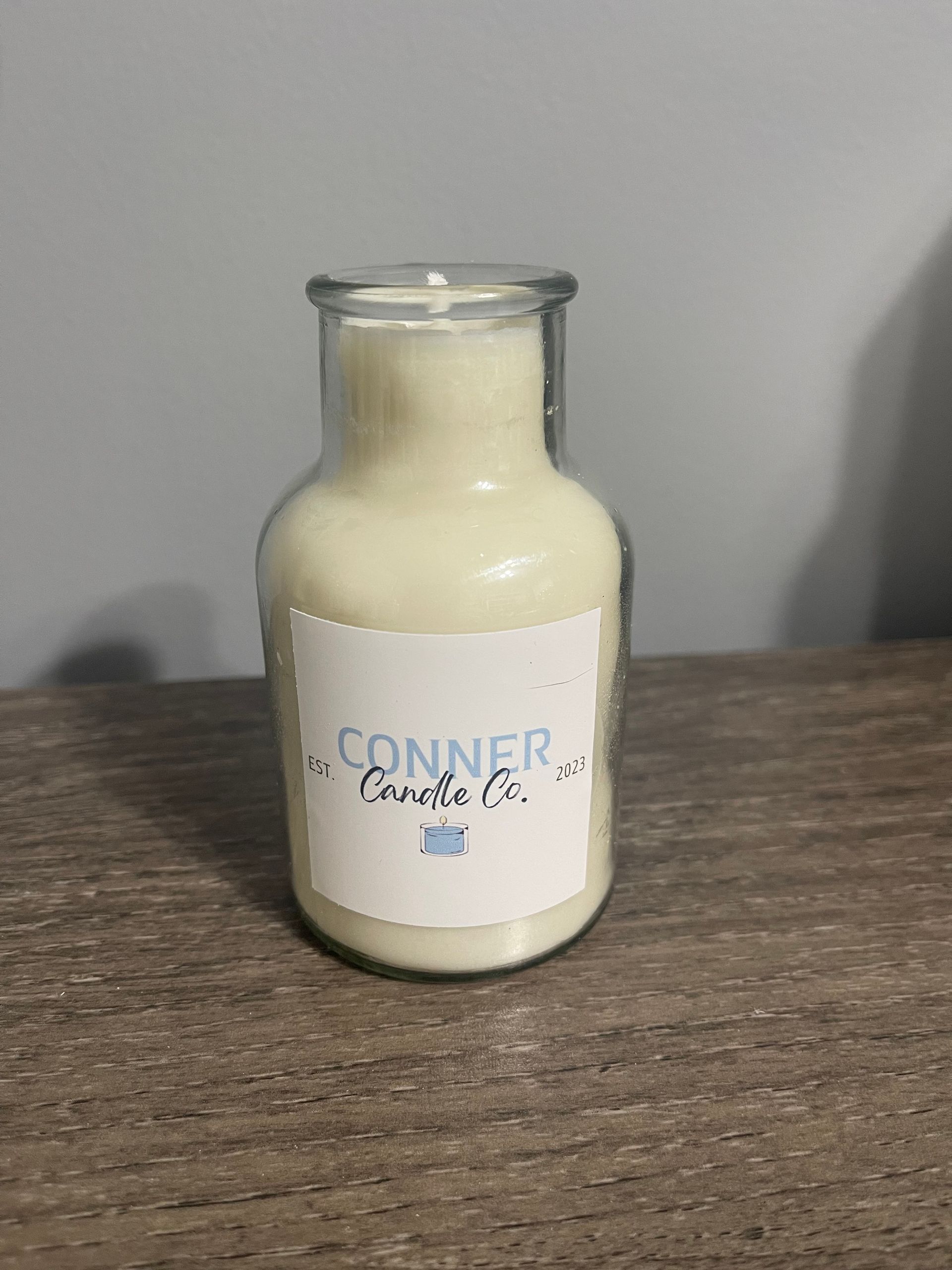 Cream-colored candle in a clear glass bottle, labeled 