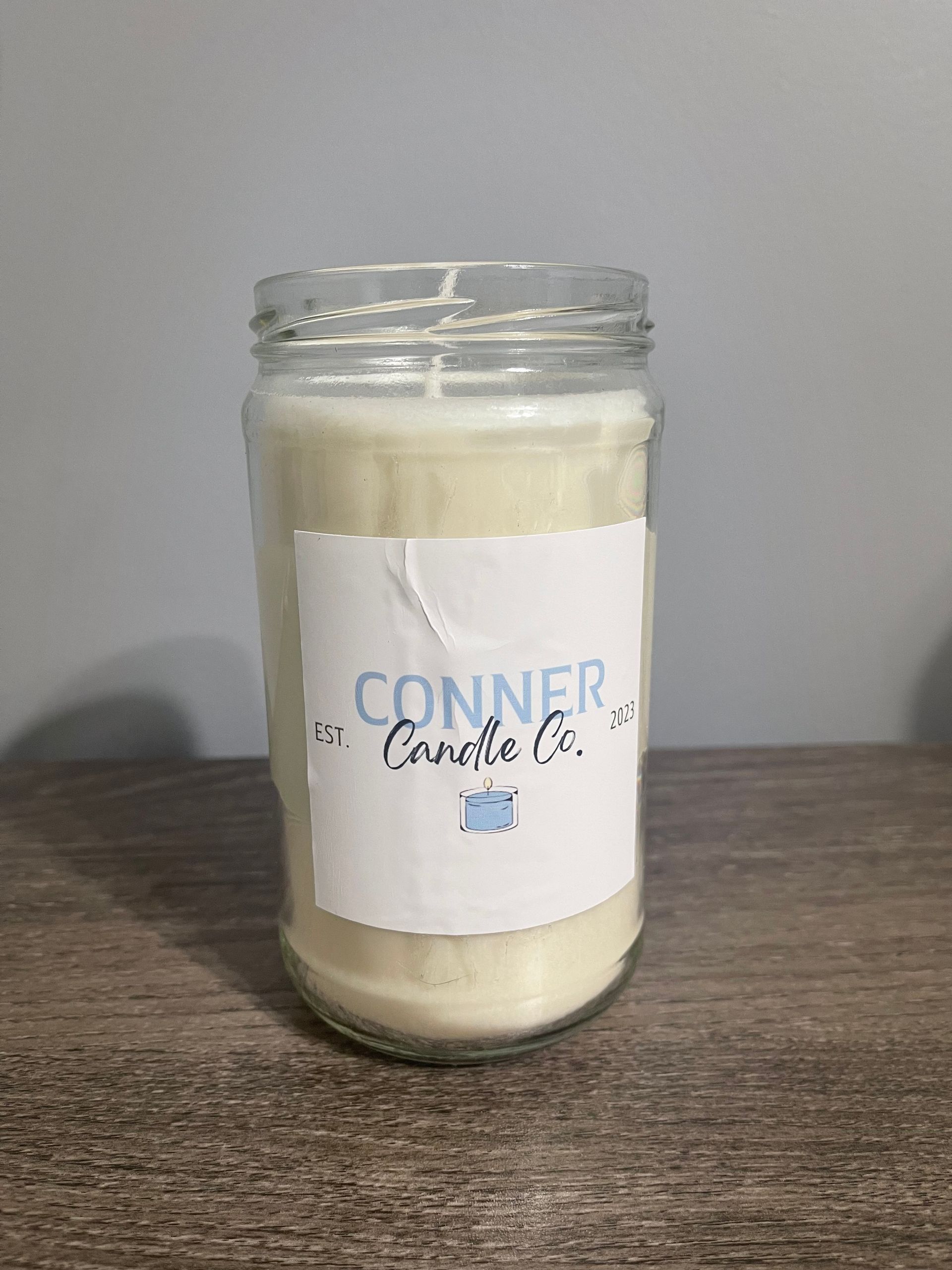 Cream-colored candle in a clear glass jar with a white label reading 