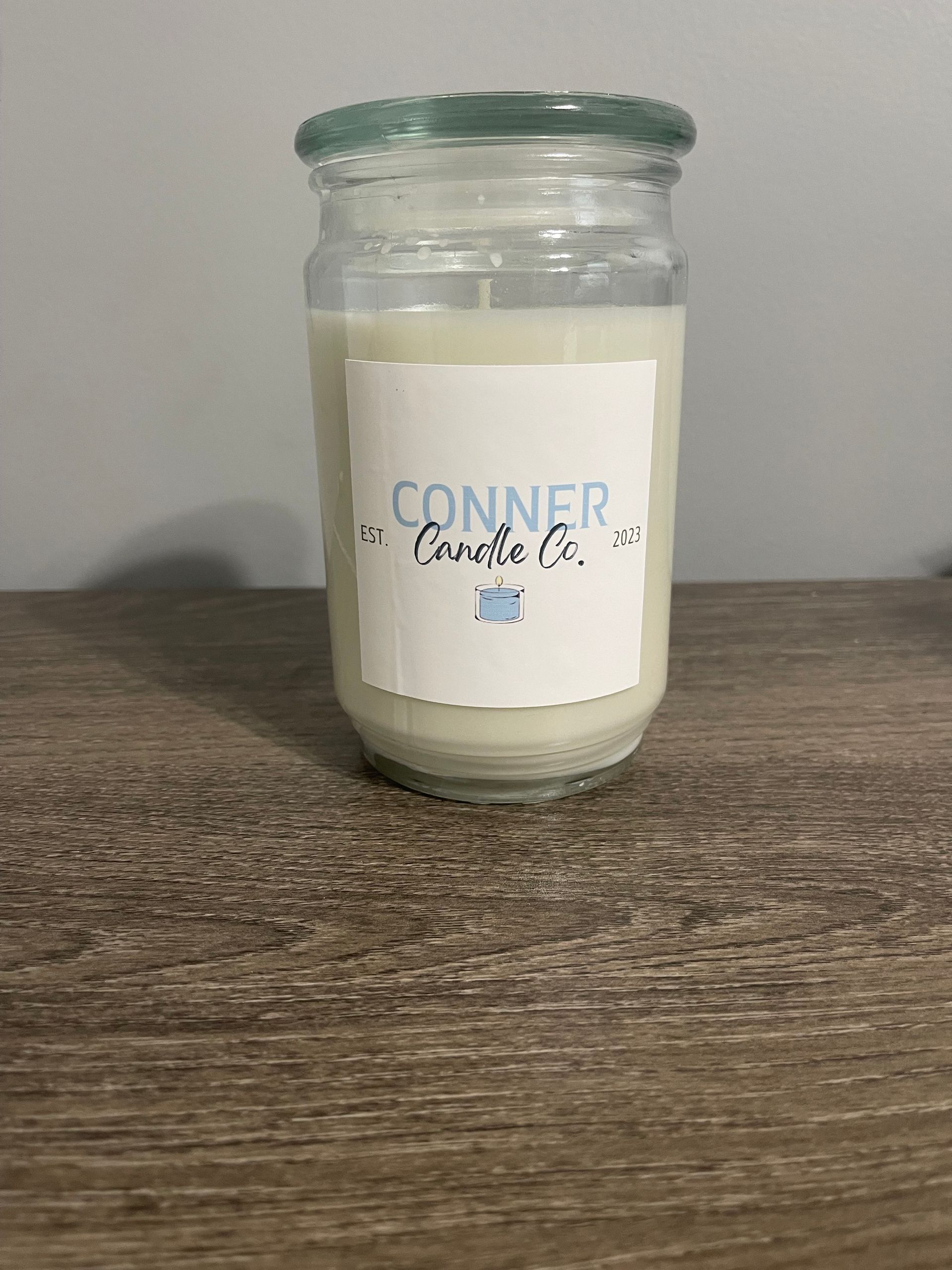 A white candle in a clear glass jar with a label that reads 