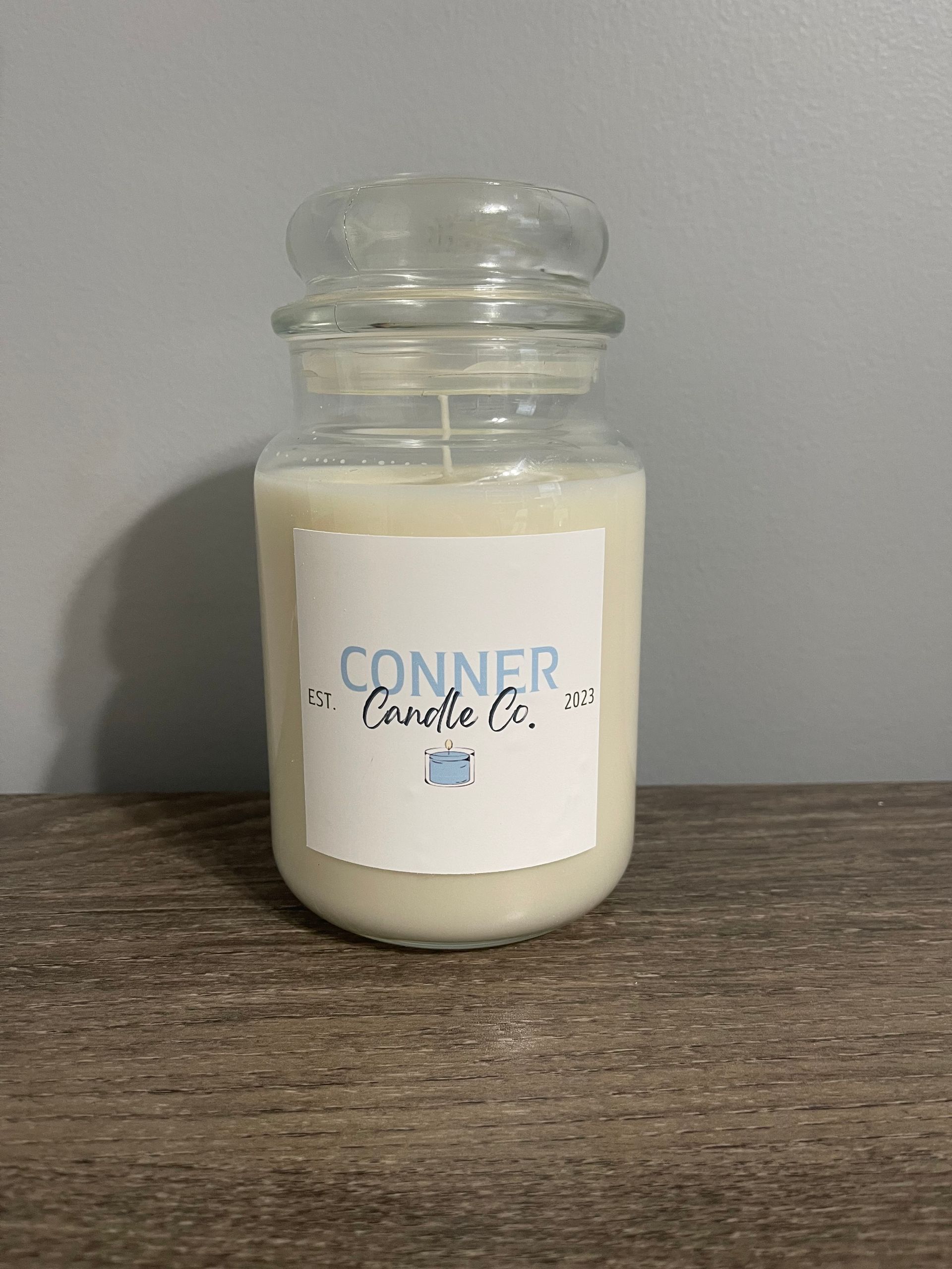 A candle in a glass jar with a lid. It has a white label with 