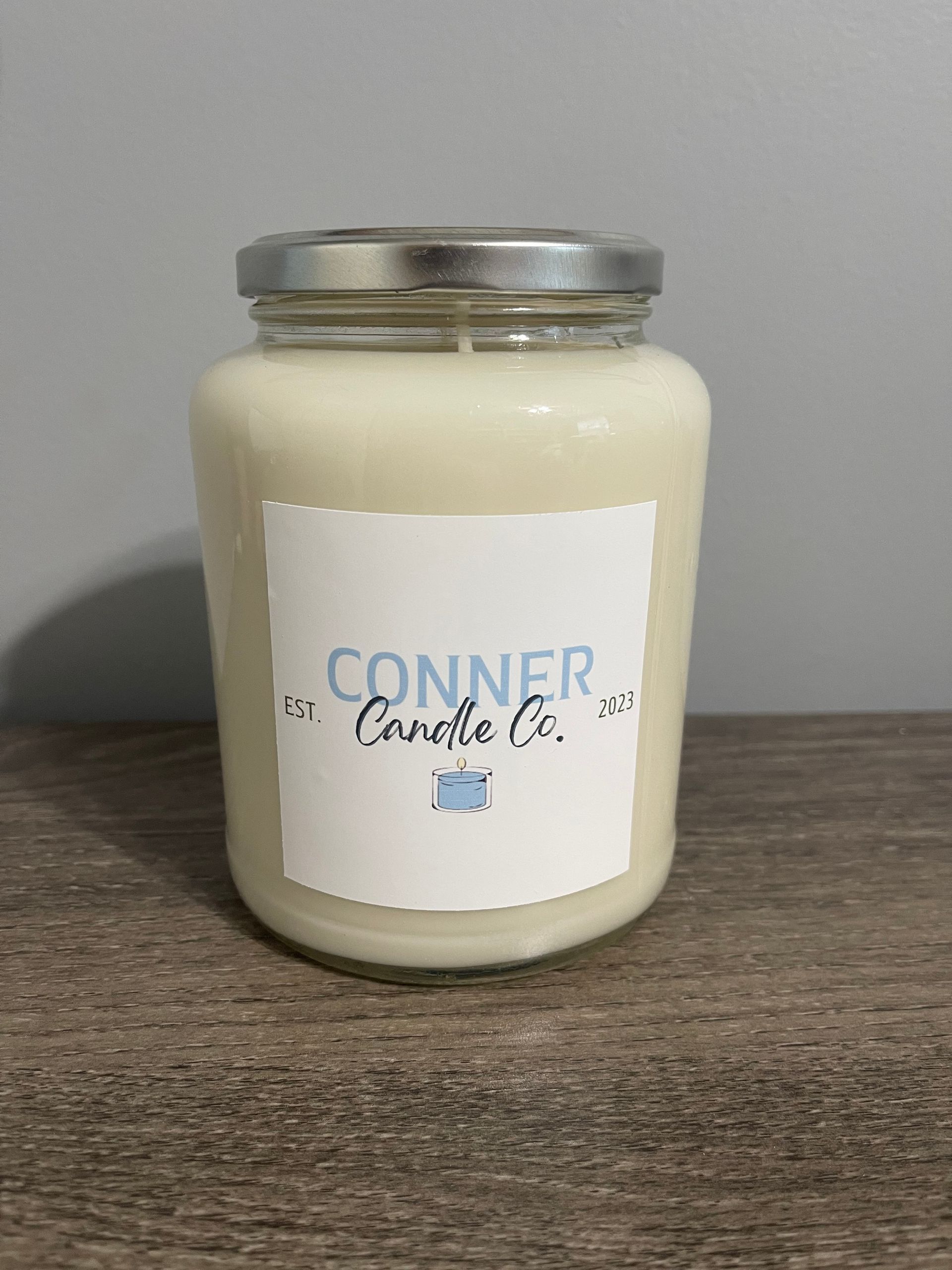 Cream-colored candle in a glass jar with a silver lid. A label reads 