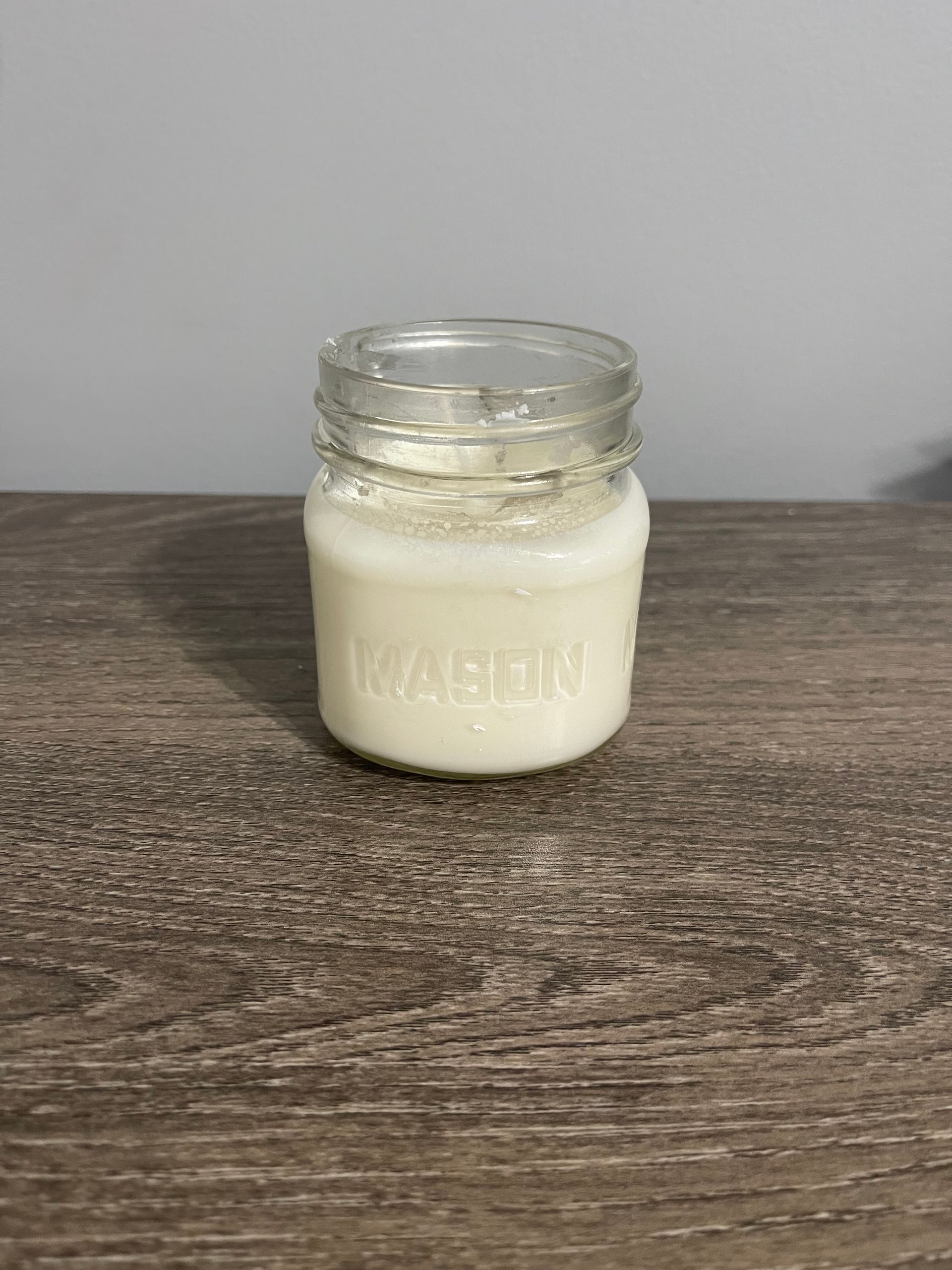 Small glass jar filled with white, opaque liquid on a brown wooden surface. The jar is labeled 