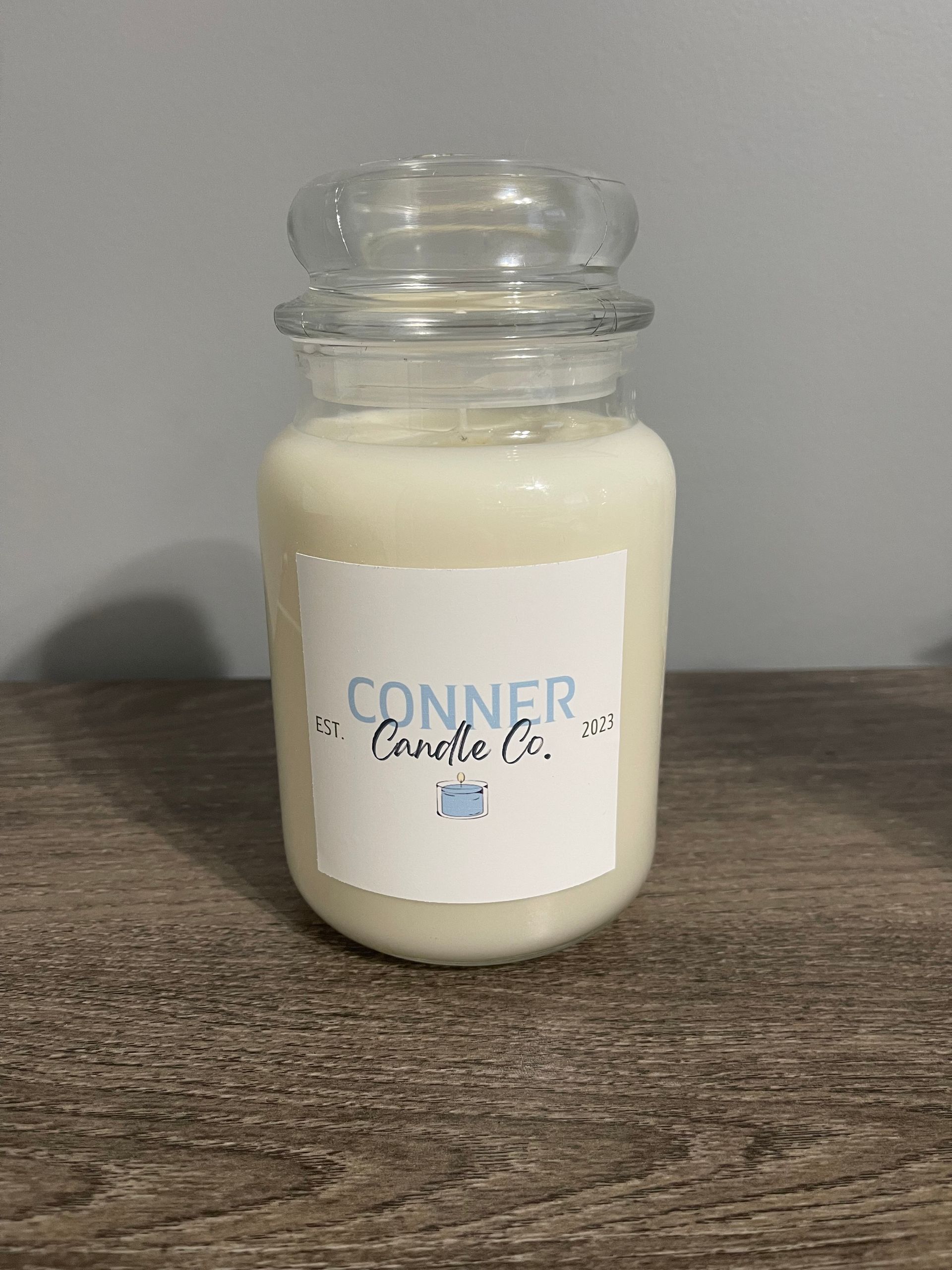A white candle in a glass jar with a label that says 