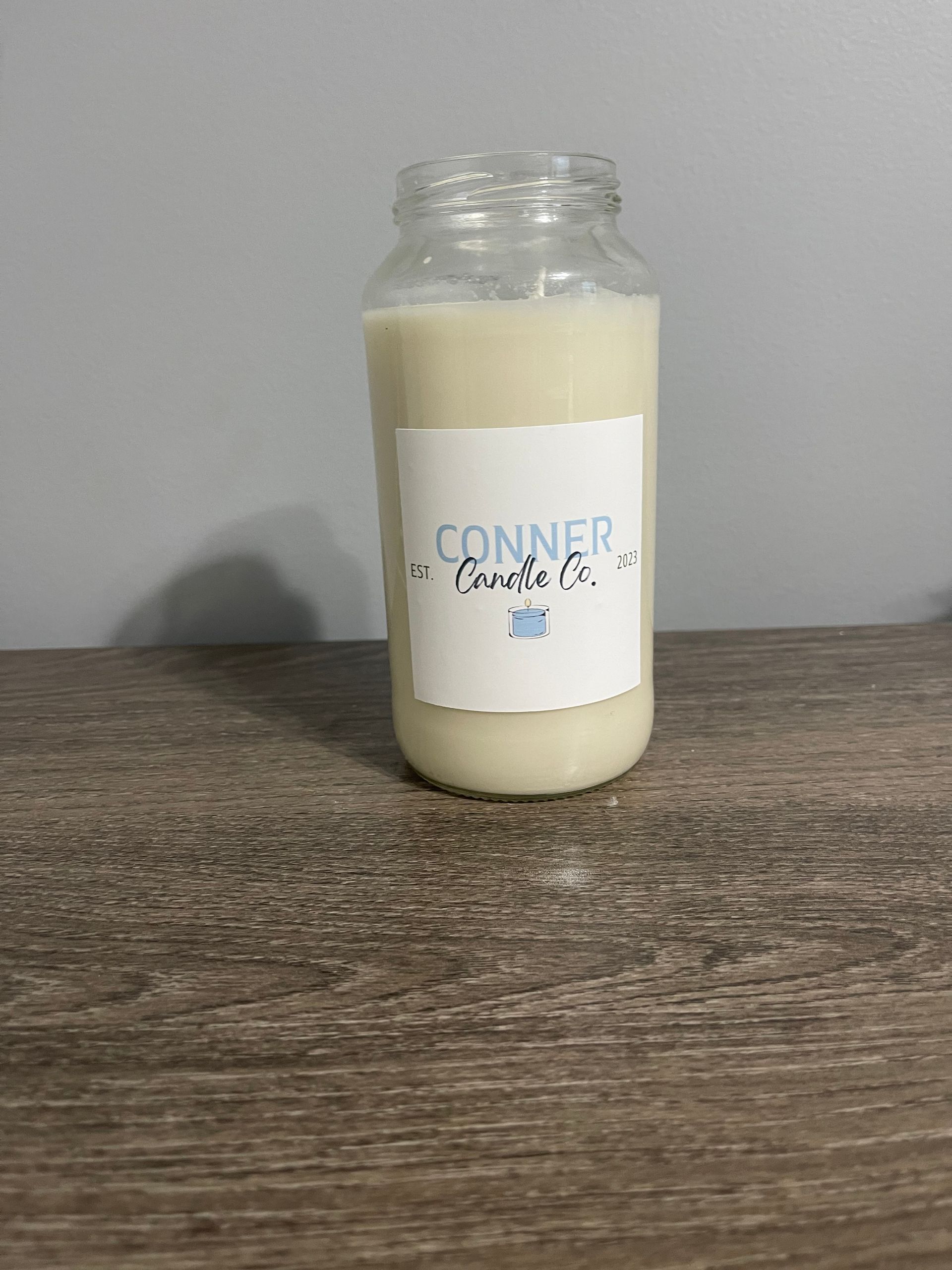 Glass jar candle with "Conner Candle Co." label on a wooden surface.