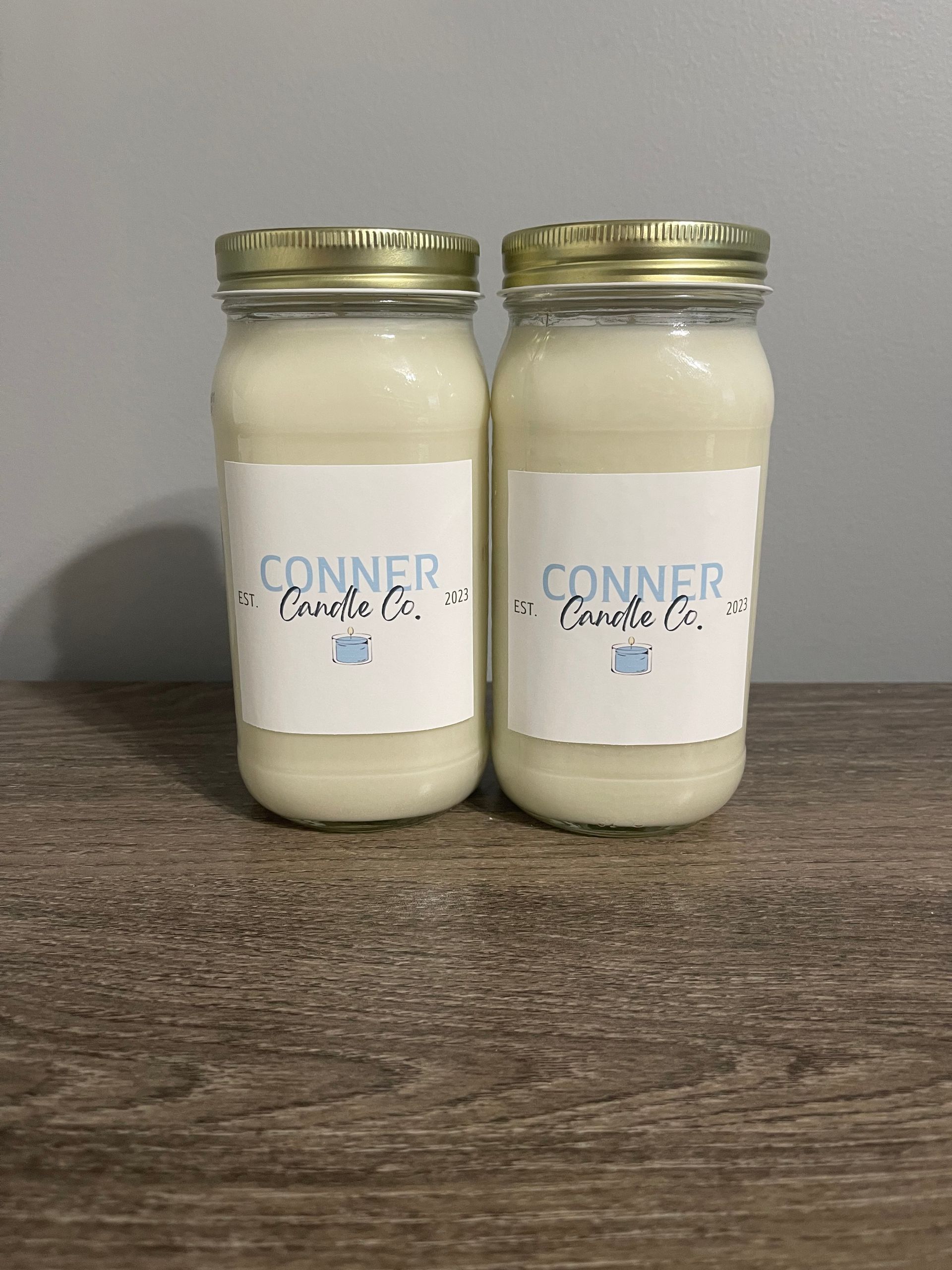 Two jars of Conner Creek Co. products on a wooden surface, with white labels and gold lids.