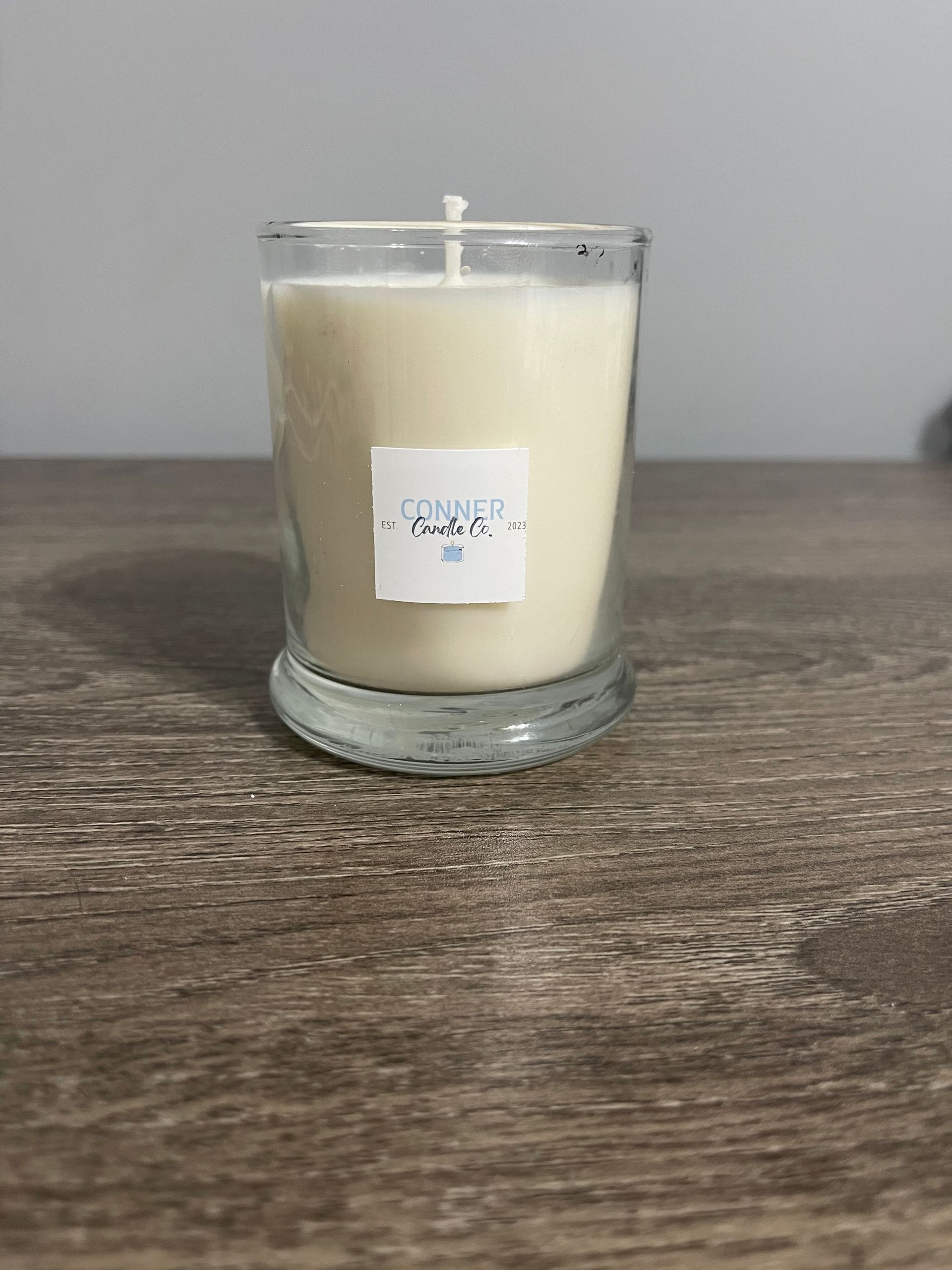 Candle in a clear glass on a wood surface, with a small label.